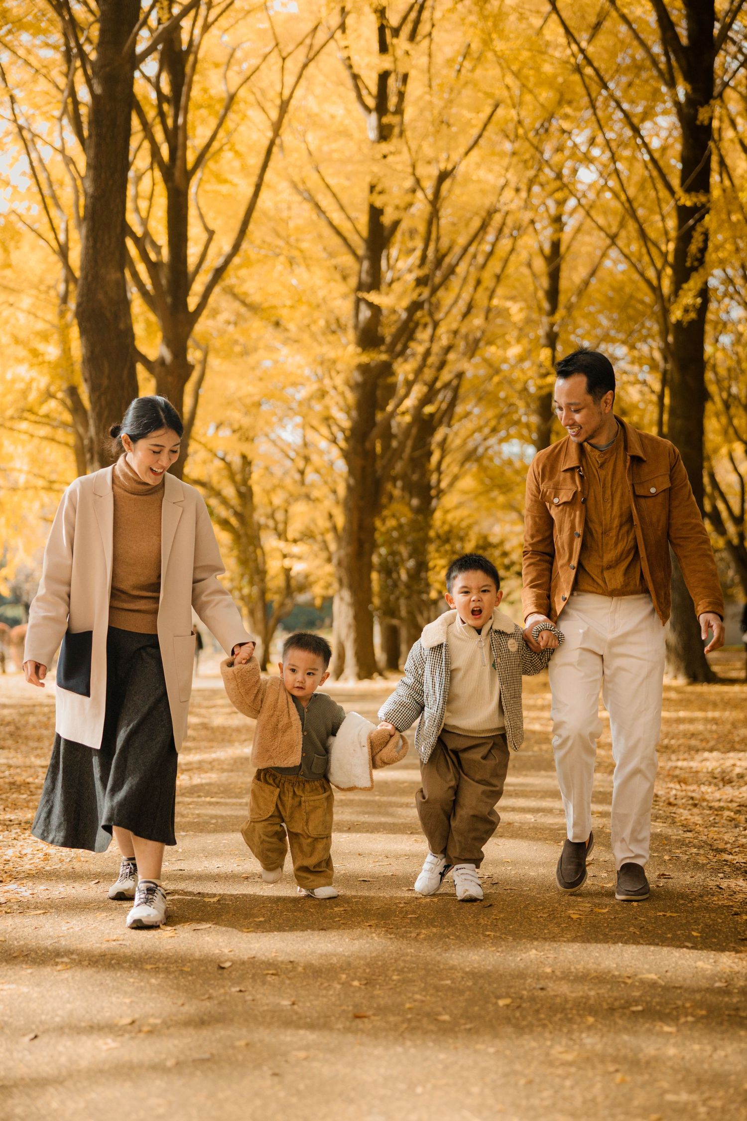 Family walking together on path lined with golden autumn trees.