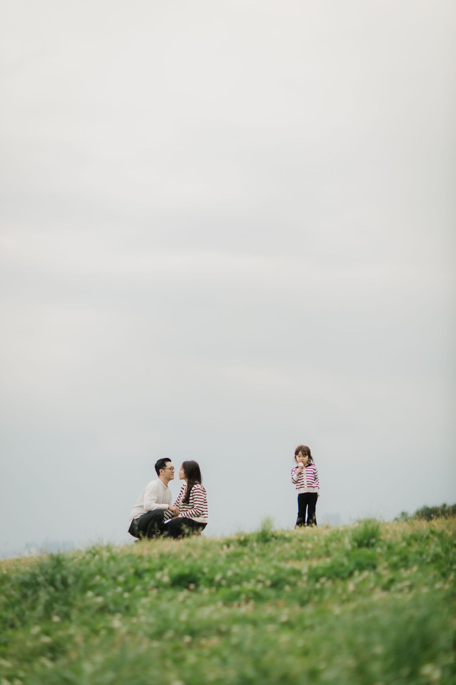 People sitting on grassy hilltop against cloudy sky.