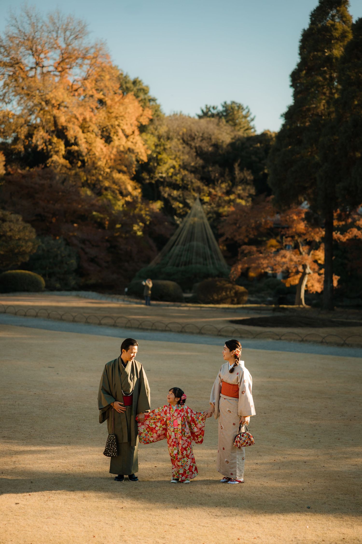A traditional Japanese family in kimonos strolls through a serene autumn garden with golden foliage.