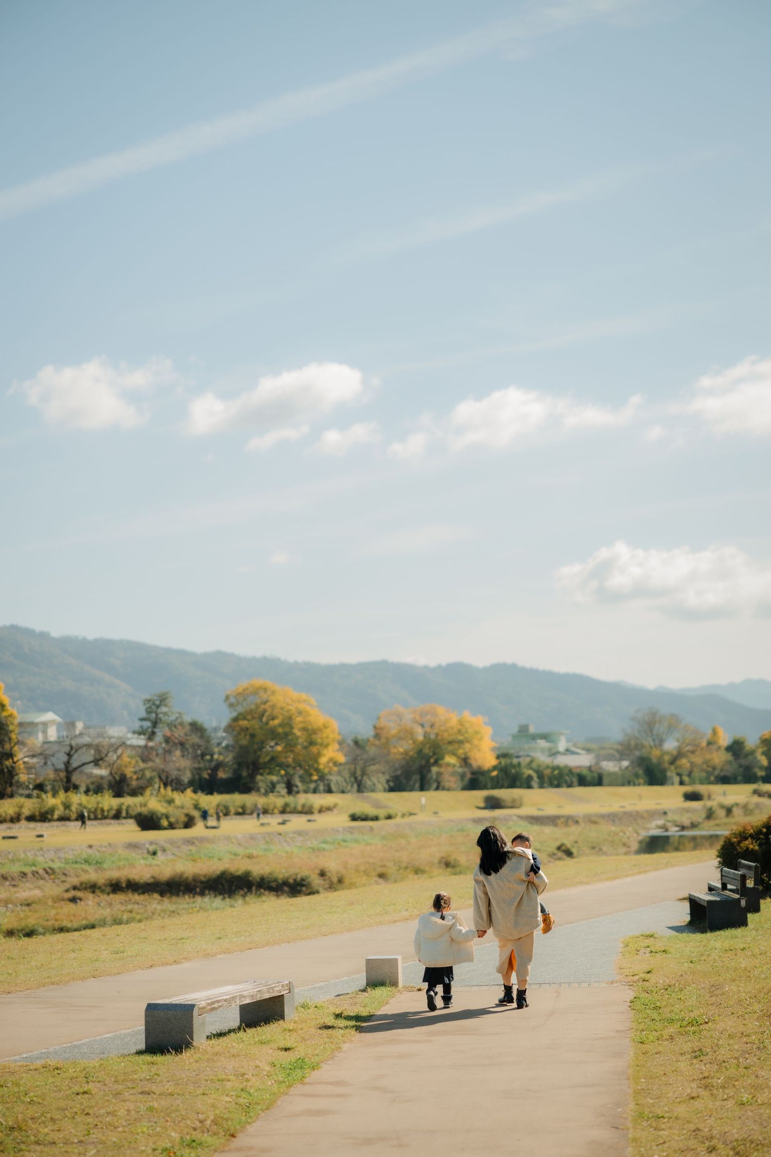 People walking on paved path through autumn countryside landscape.