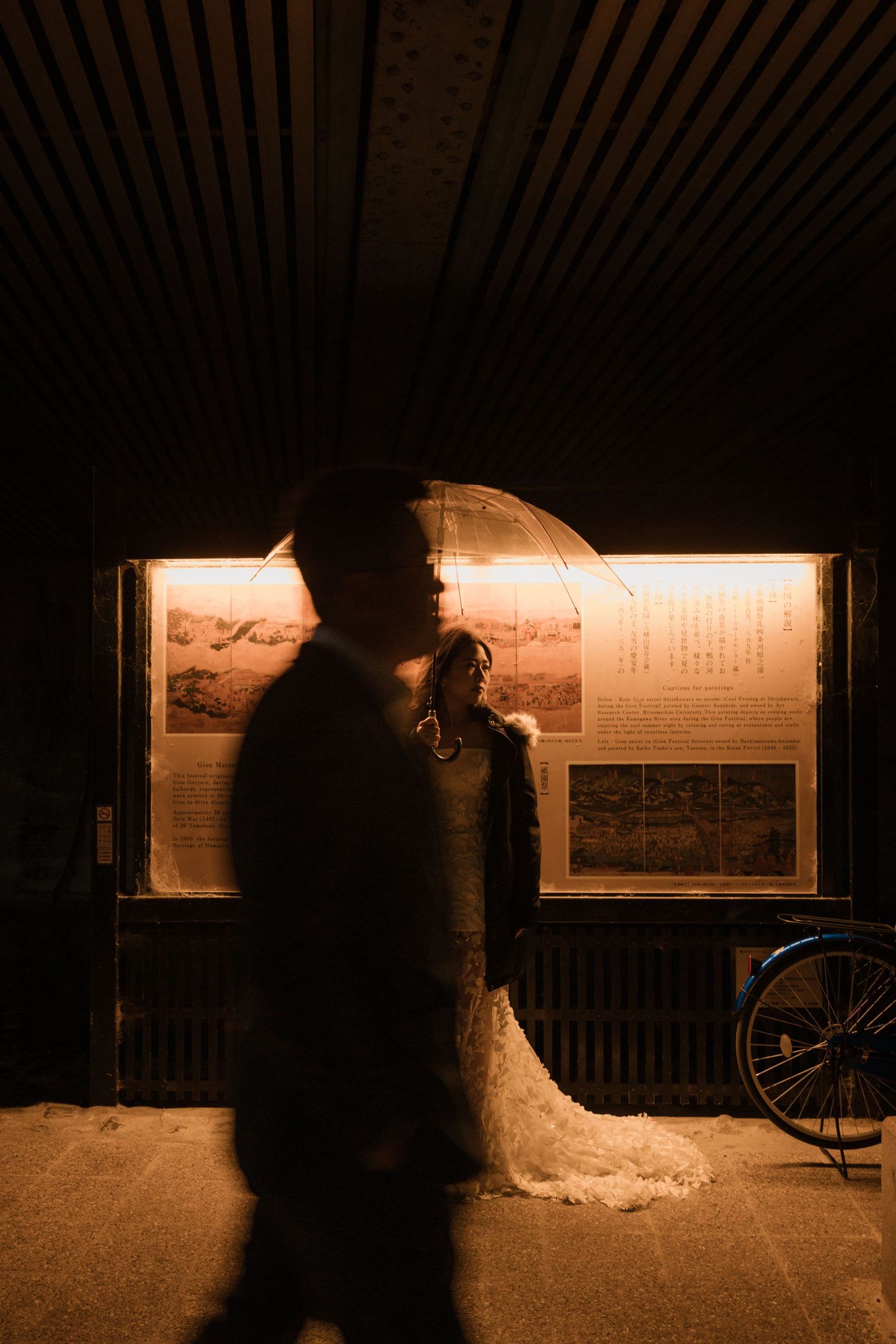Silhouetted couple stands in warm lighting against illuminated display boards at night.
