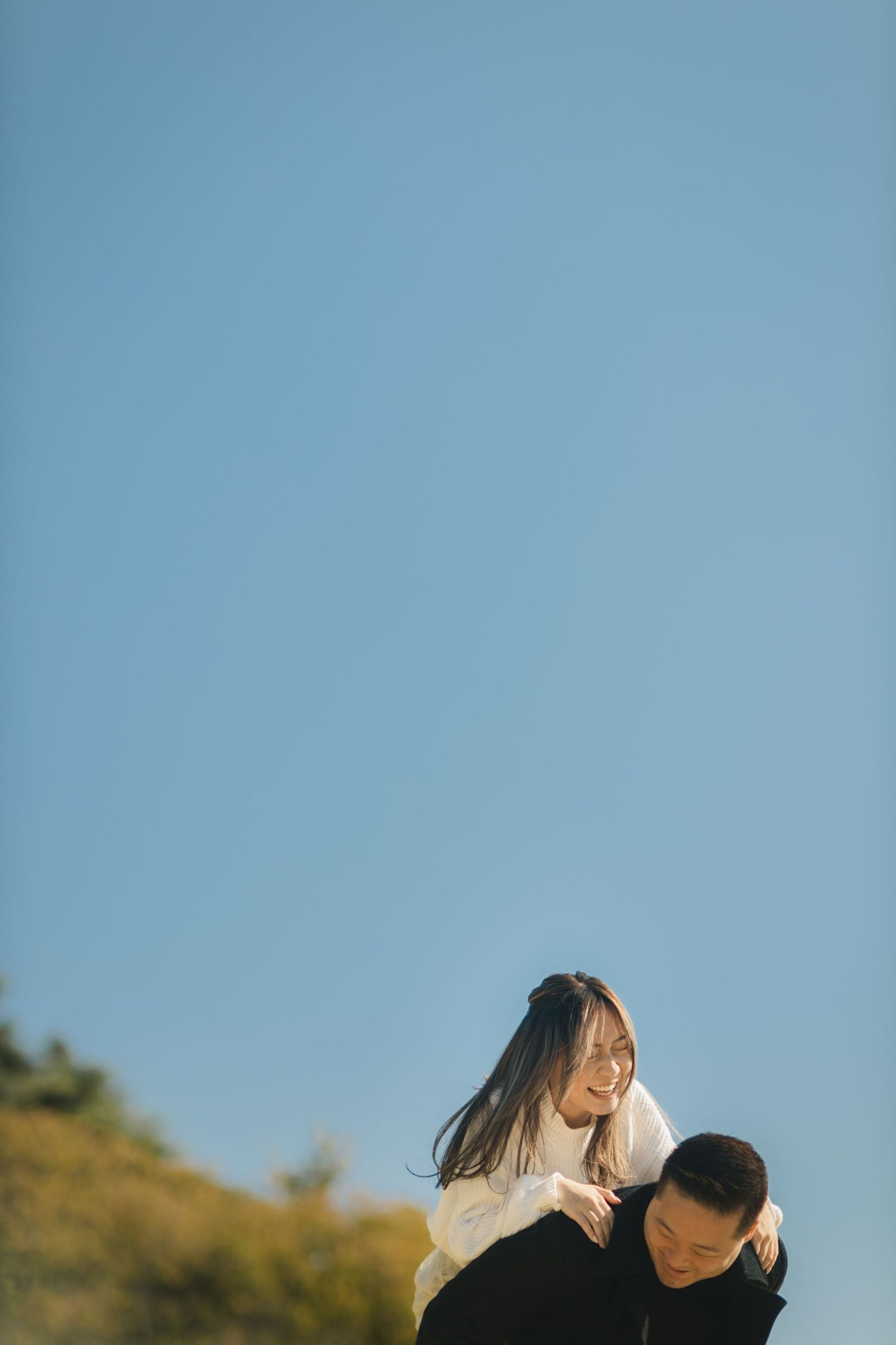 A romantic outdoor photoshoot featuring a couple sharing a joyful moment against a blue sky backdrop.