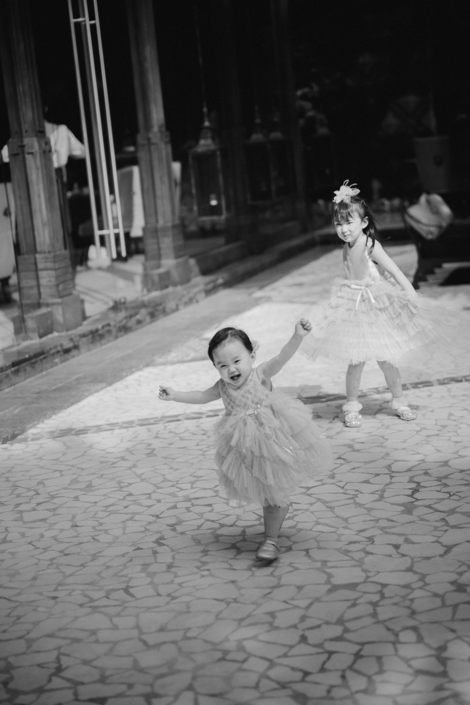 Children in tulle dresses dancing on paved street in black and white photograph.