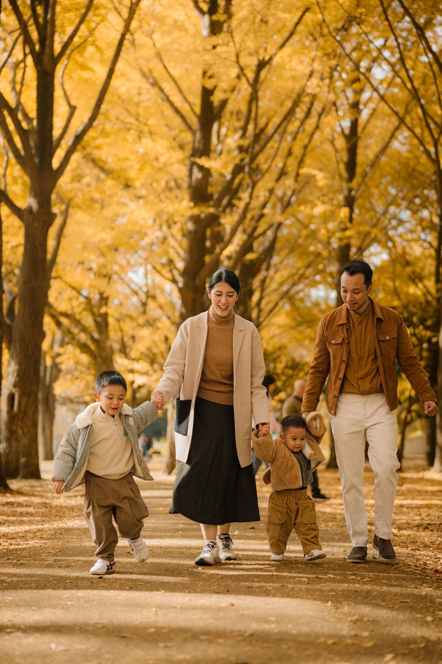A family walking together on a path lined with golden yellow autumn trees.