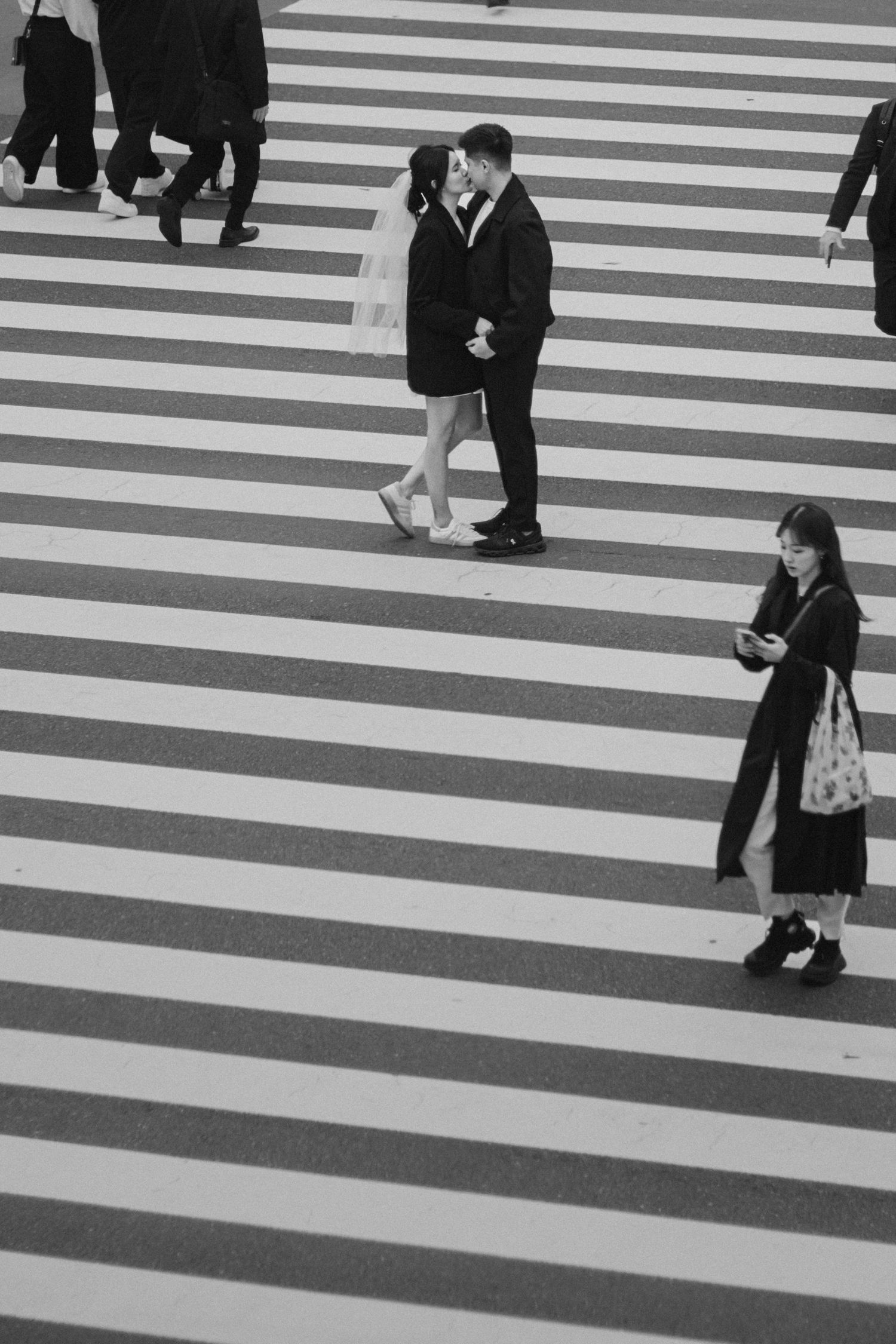 People crossing a geometric black and white striped crosswalk in an urban setting.