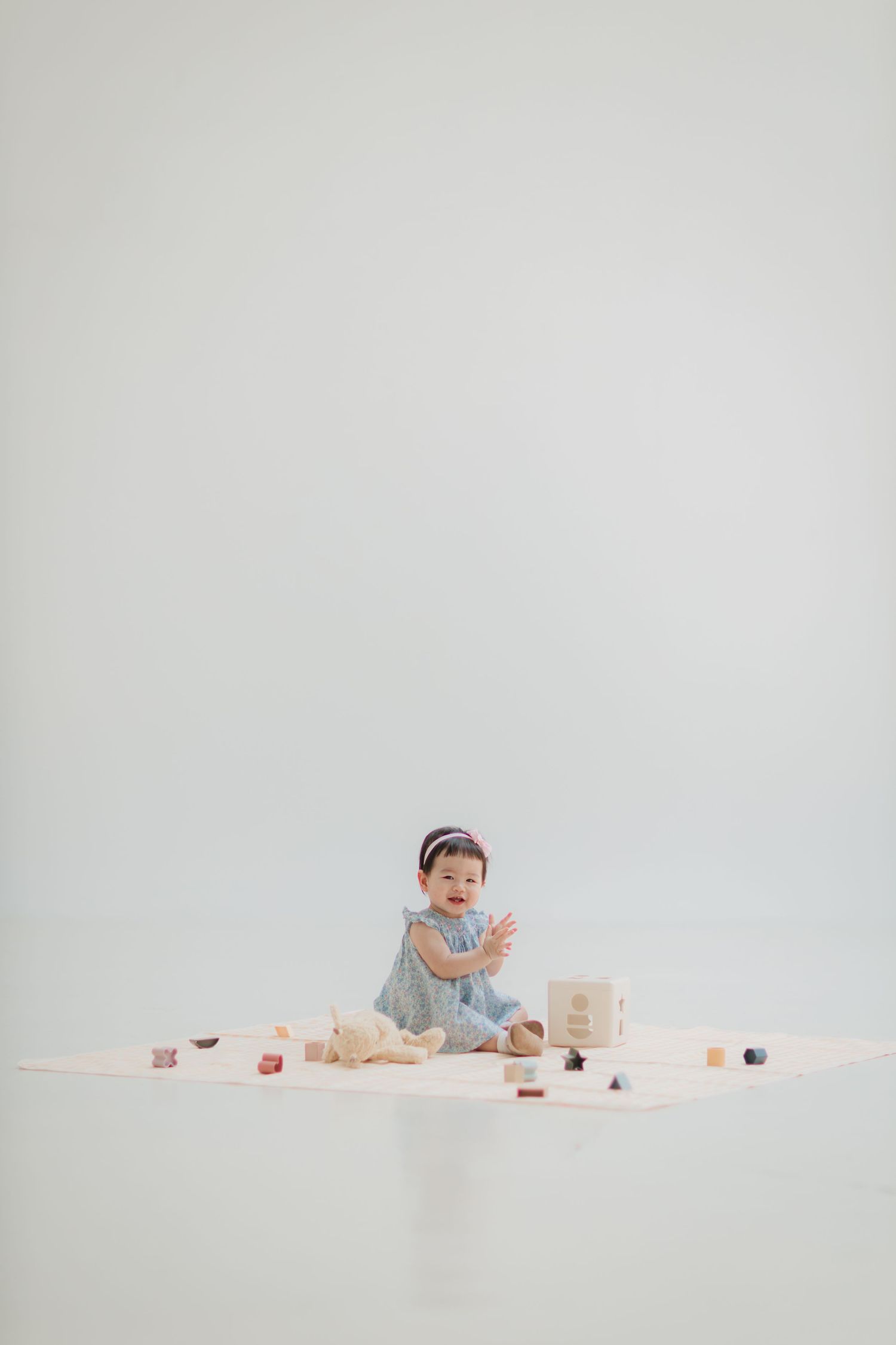 Small child sits surrounded by toys on white background in minimalist setting.