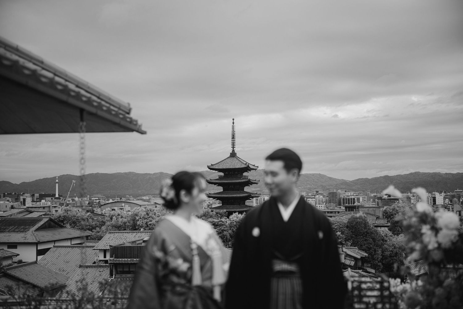 A black and white scene with two people in traditional Japanese clothing overlooking Kyoto with a pagoda in the background.