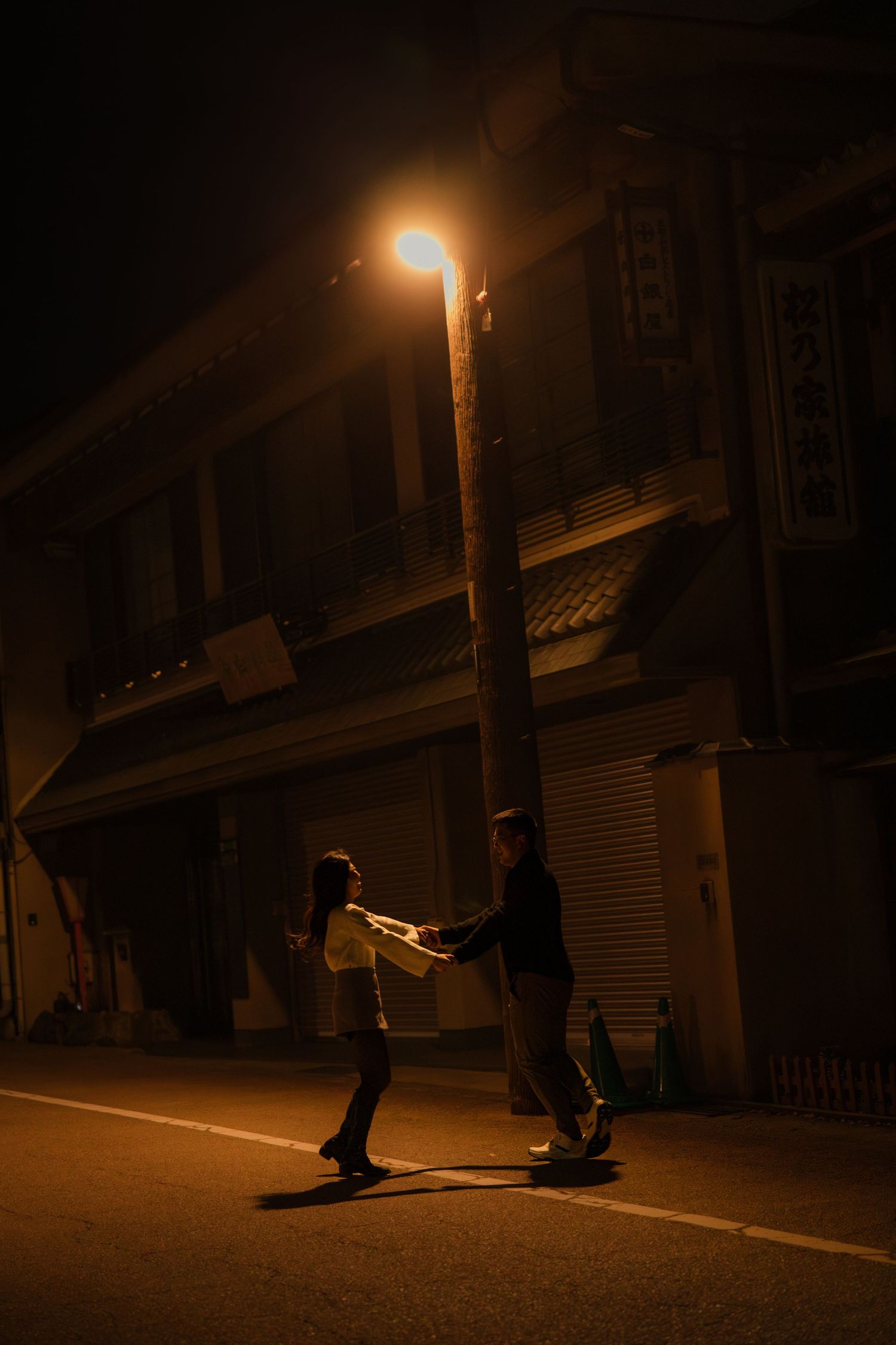 A nighttime street scene with two people beneath a glowing streetlamp.