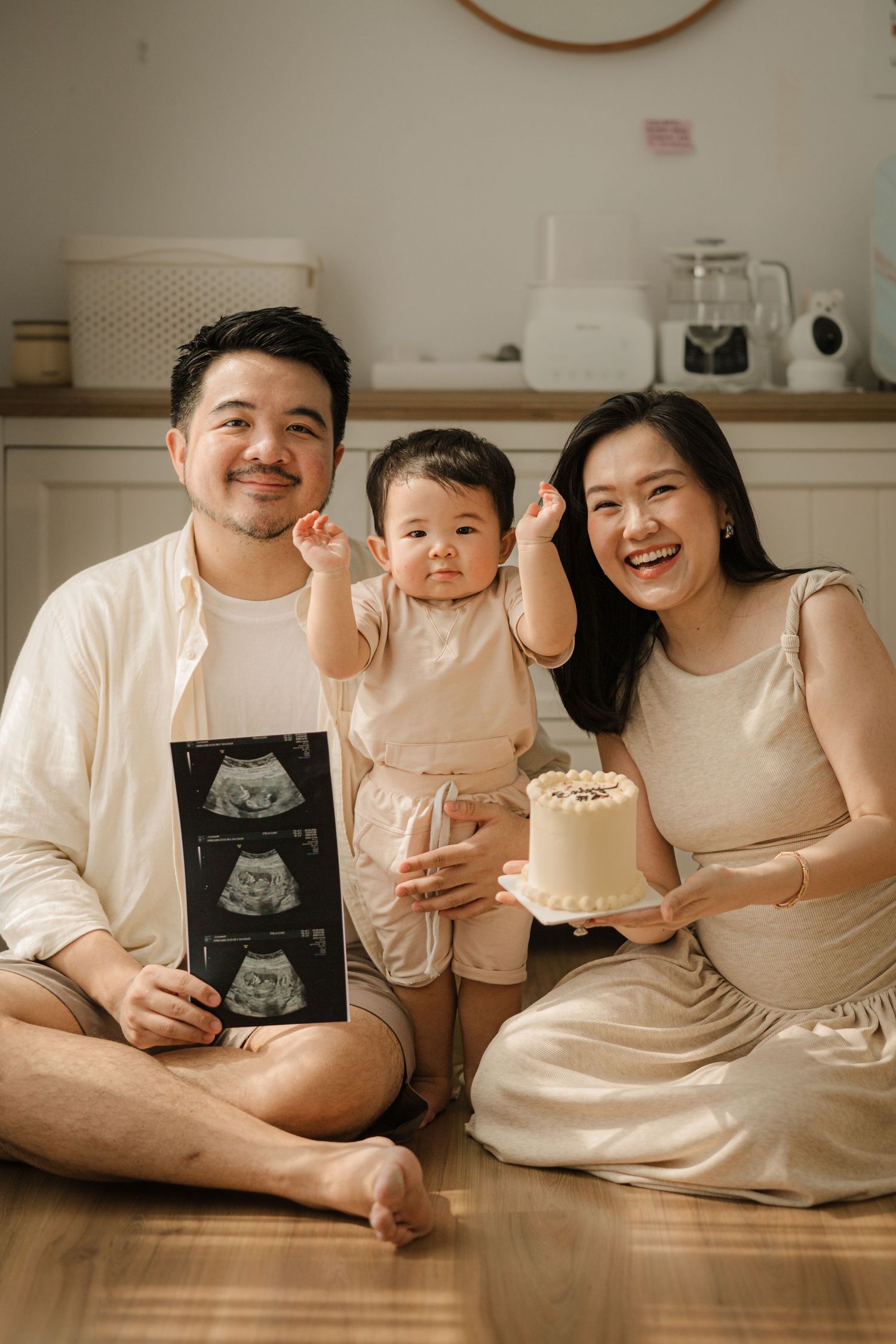 Family celebrating pregnancy announcement with ultrasound photos and small cake on floor.