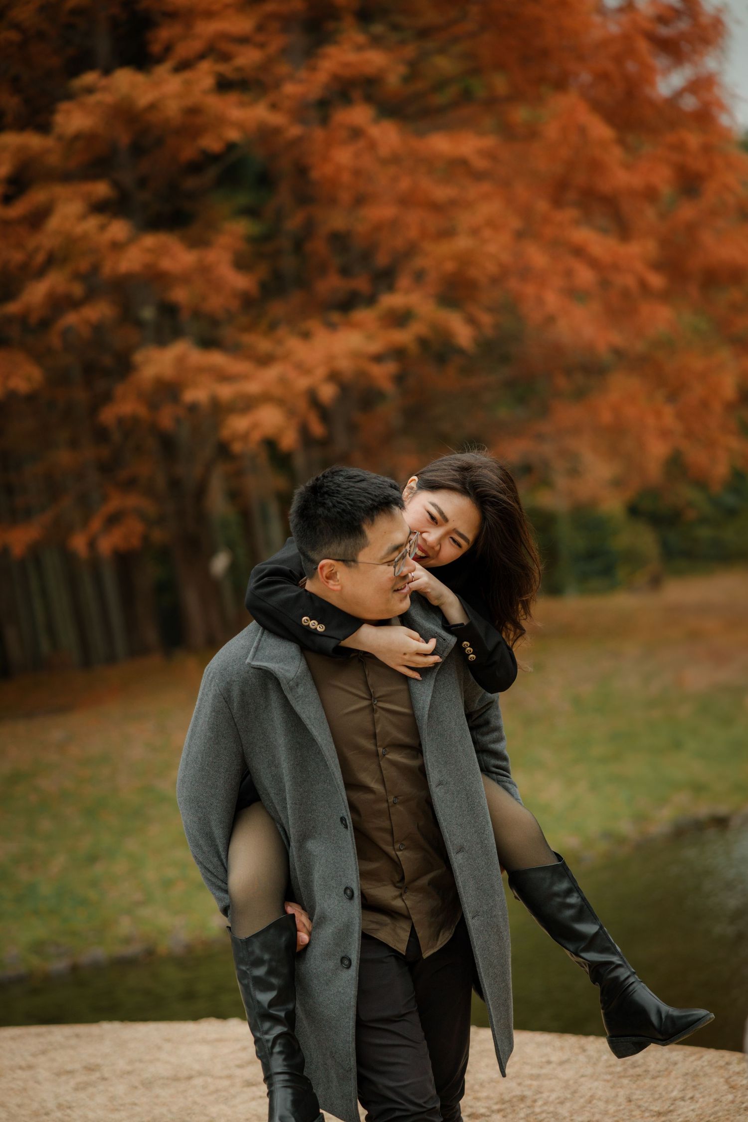 A playful autumn scene with one person giving another a piggyback ride among orange trees.