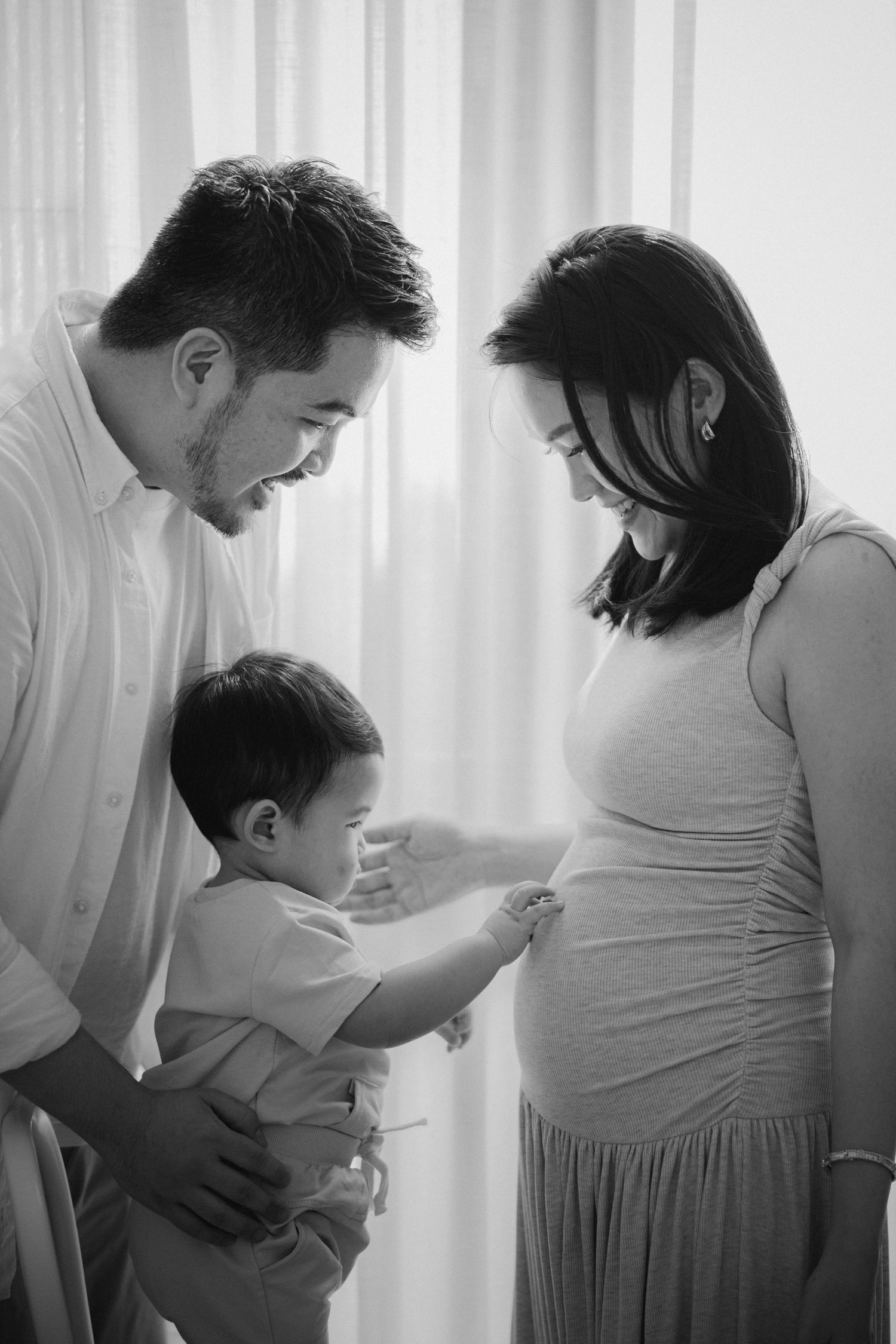 Tender family moment with expecting parents and young child in window light.
