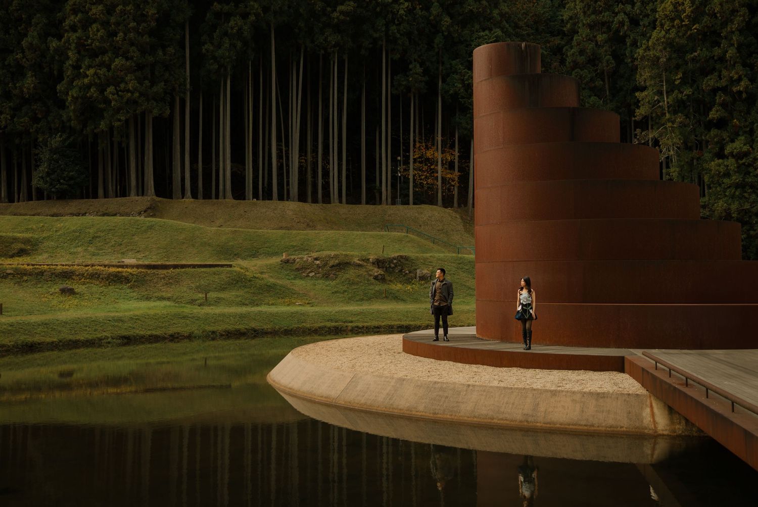 Two people stand on a curved architectural platform near a modern rust-colored structure.