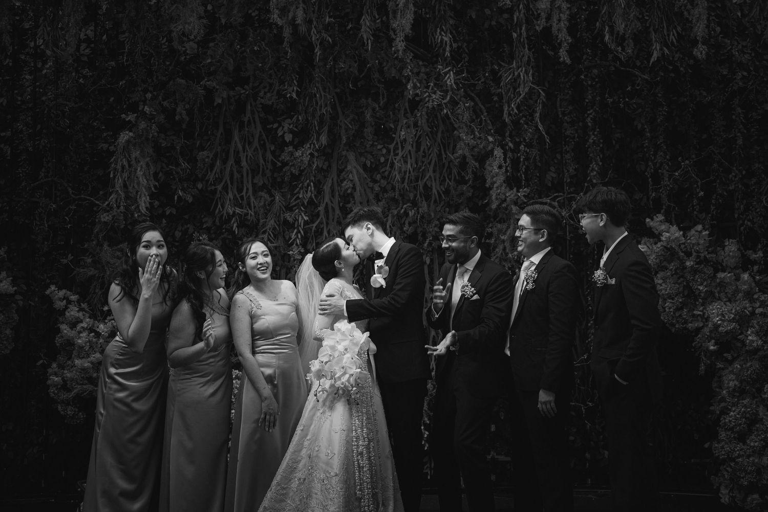 A black and white wedding party photo showing the bridal party gathered outdoors.