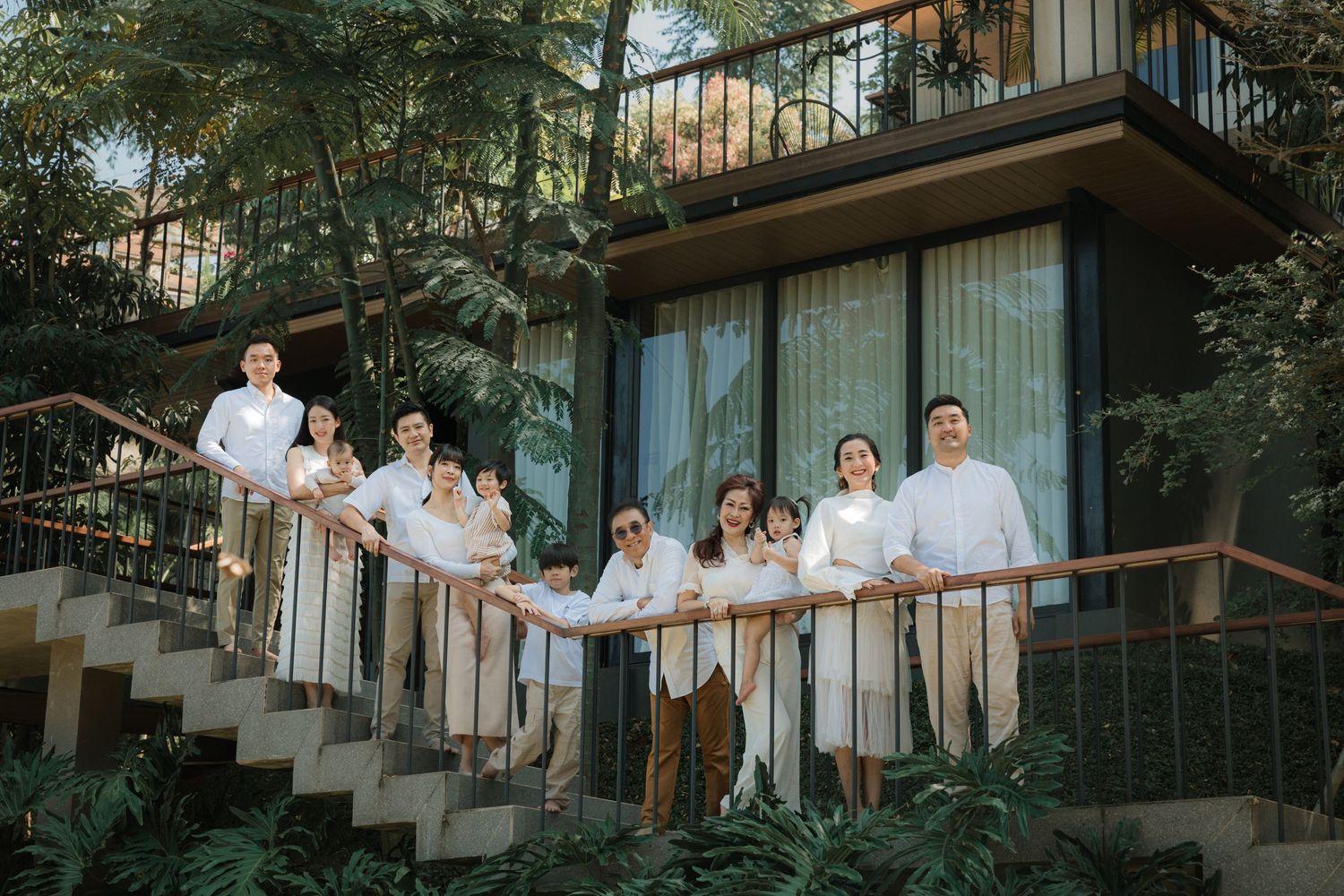 A group poses together on the exterior staircase of a modern house surrounded by greenery.