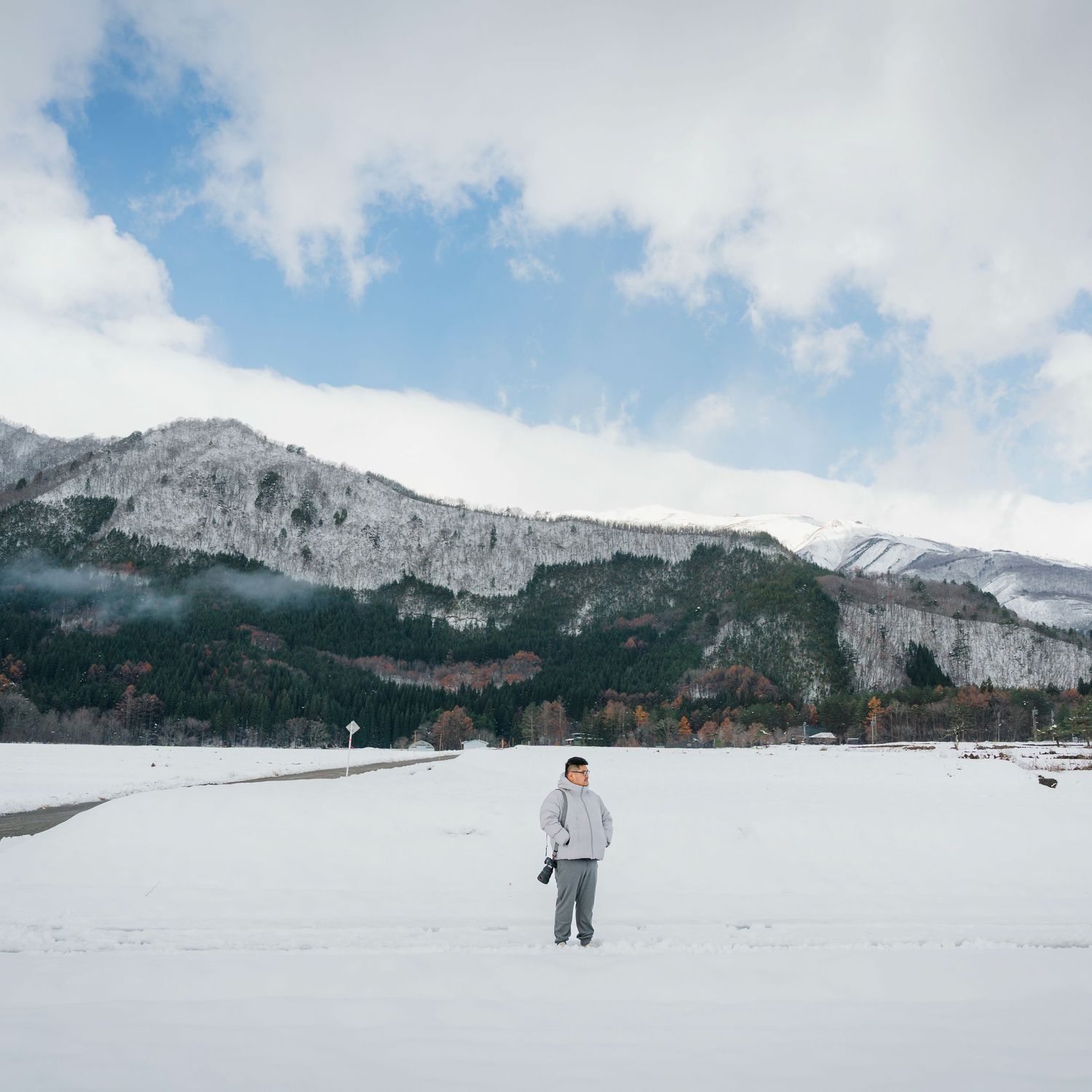 Person standing alone in snowy field with dramatic mountain backdrop.