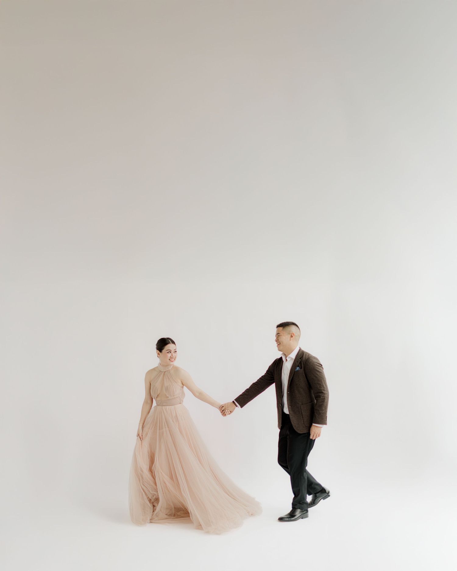 A couple in formal attire moving gracefully against a minimalist white studio backdrop.