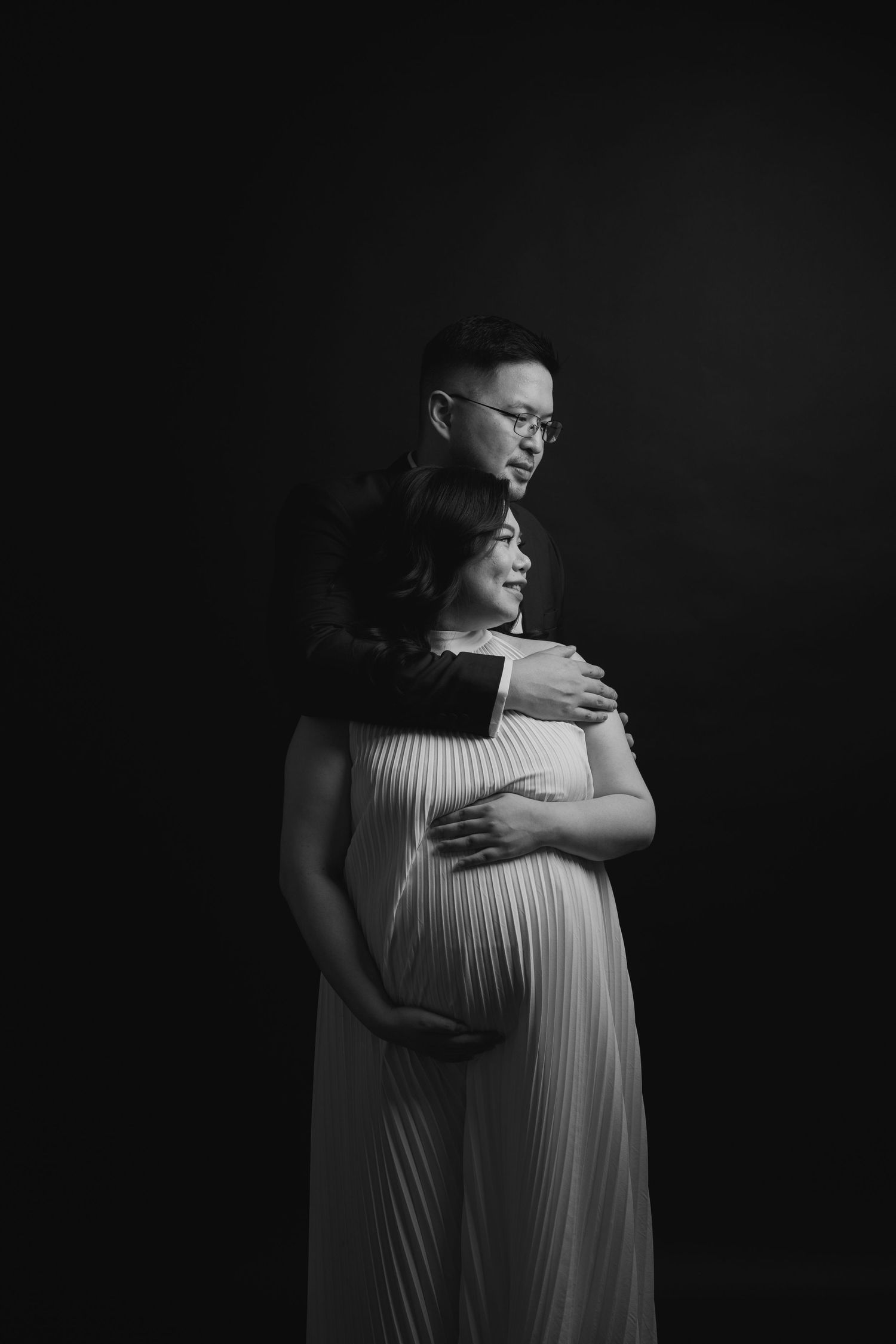 Artistic black and white maternity portrait with dramatic lighting.