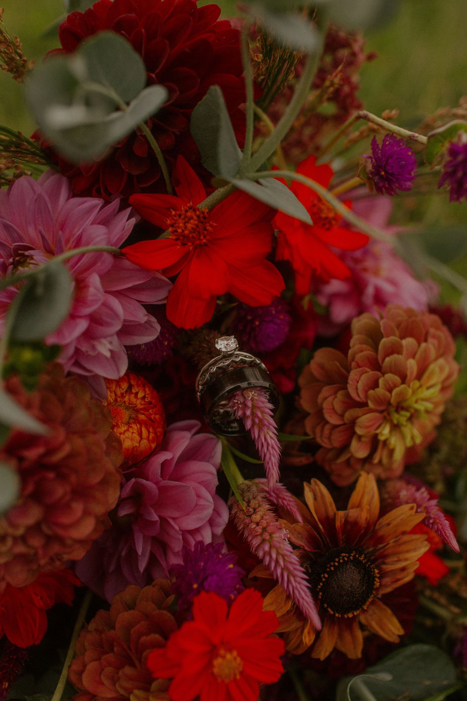 Diamond engagement ring nestled in a vibrant bouquet of red and pink flowers.