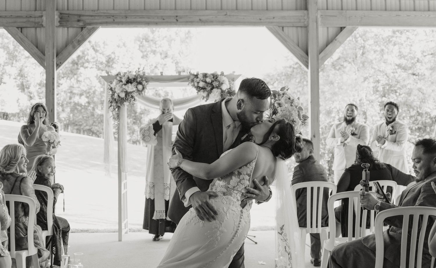 Black and white photo of bride and groom kissing passionately at wedding ceremony altar.