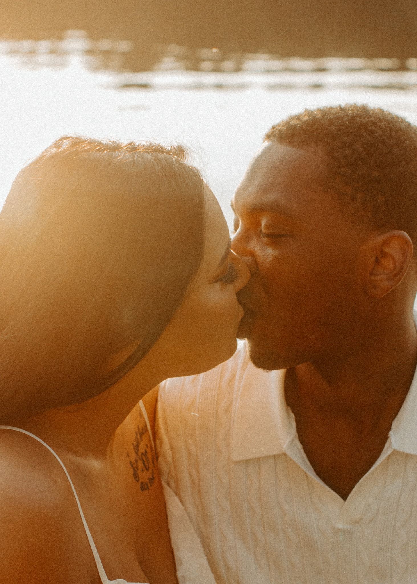 Couple sharing a golden sunset kiss near the water during a warm and intimate engagement photo session.