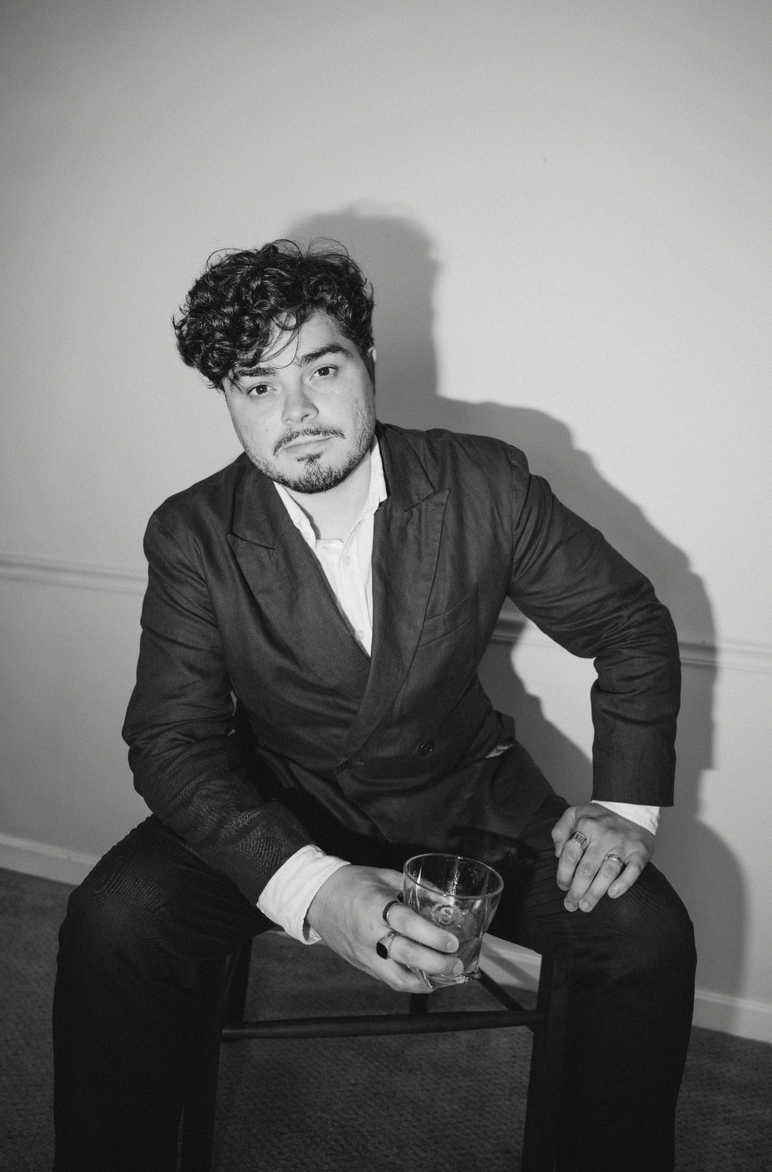 Black and white photo of a young man in a suit sitting and holding a glass of whiskey.