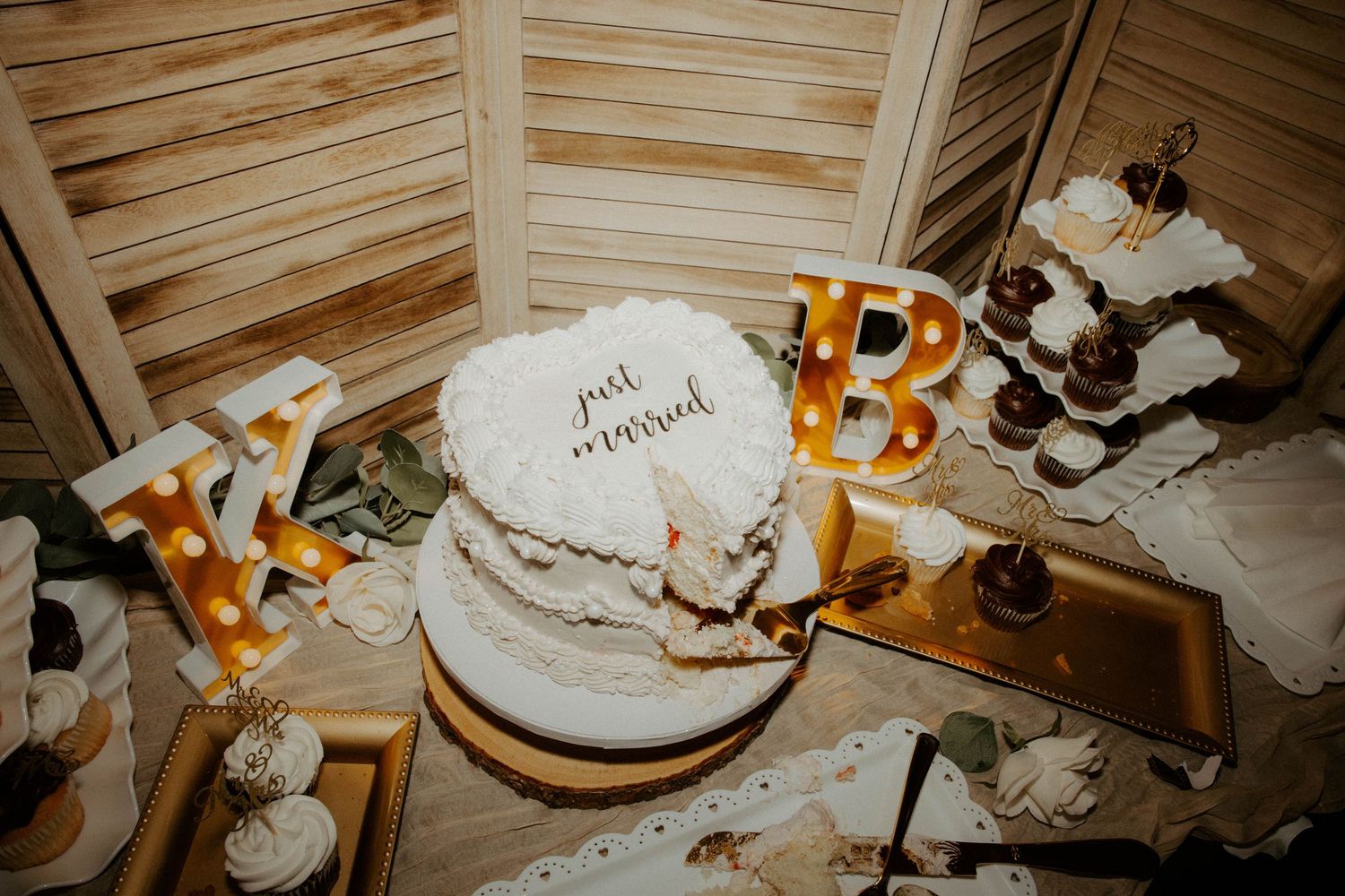 Wedding cake with just married topper displayed alongside illuminated marquee letters at reception.