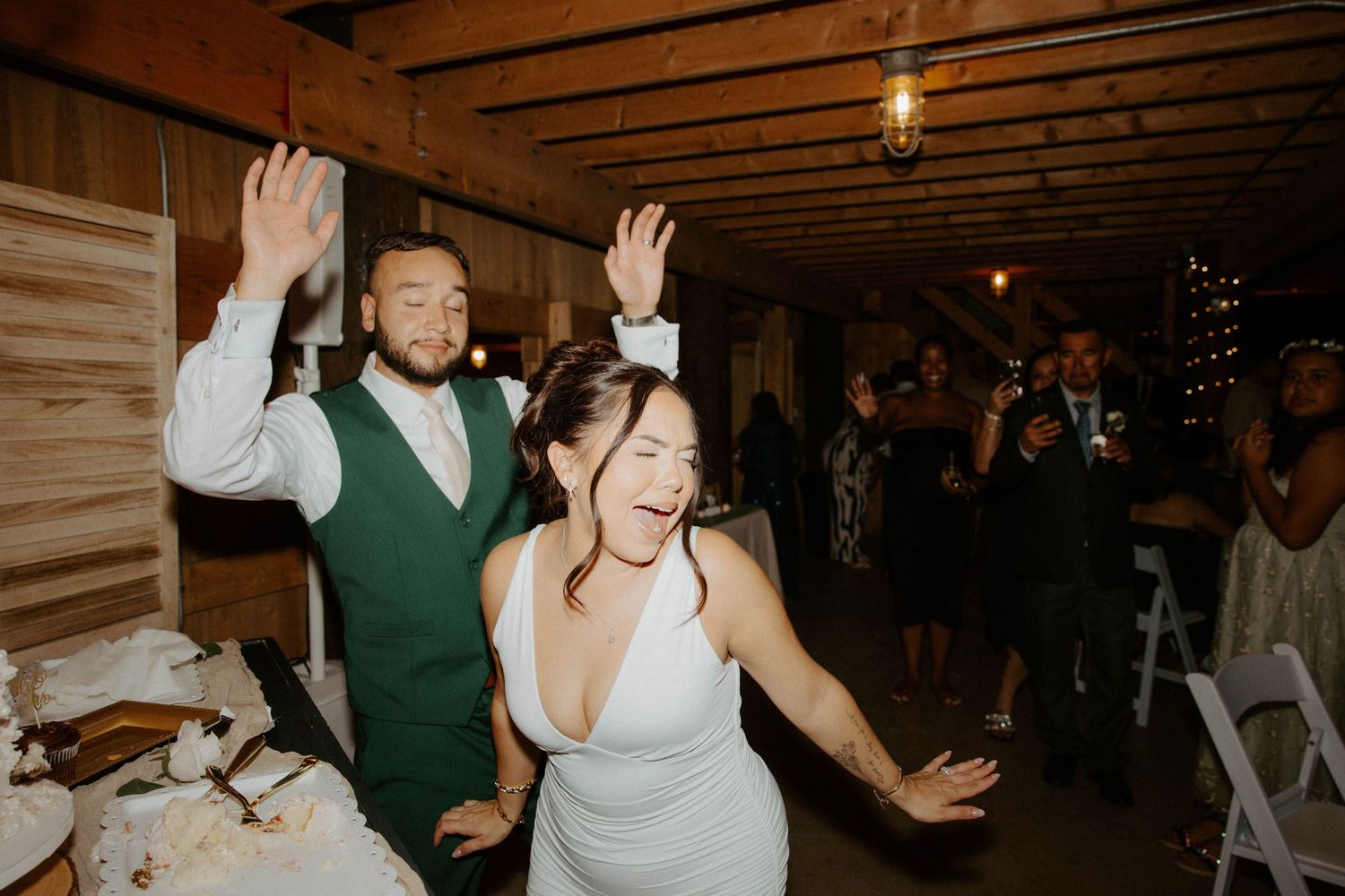 Bride and groom celebrate excitedly after cutting wedding cake at rustic barn reception.