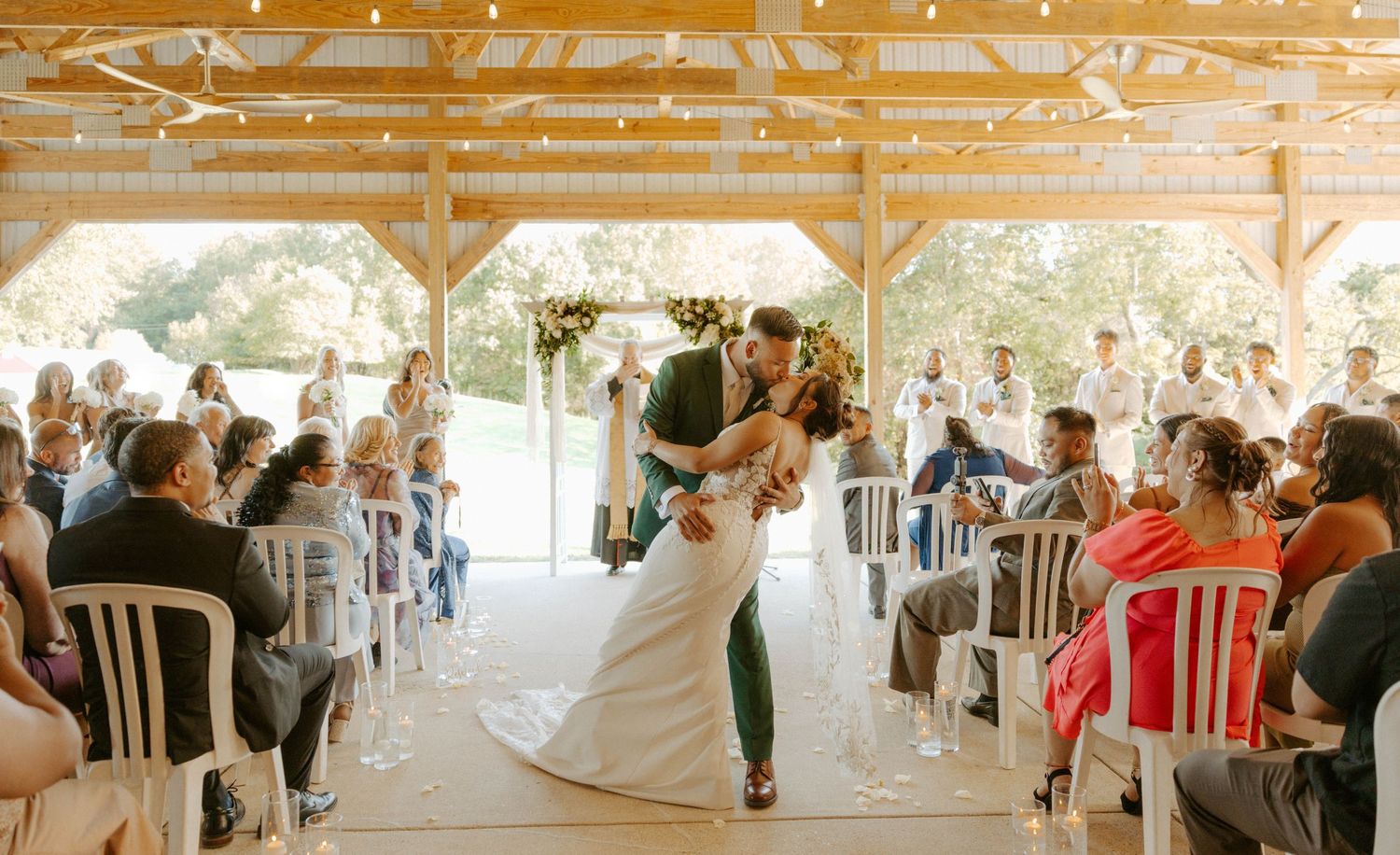 Bride and groom sharing first kiss under floral arch at outdoor pavilion wedding ceremony.