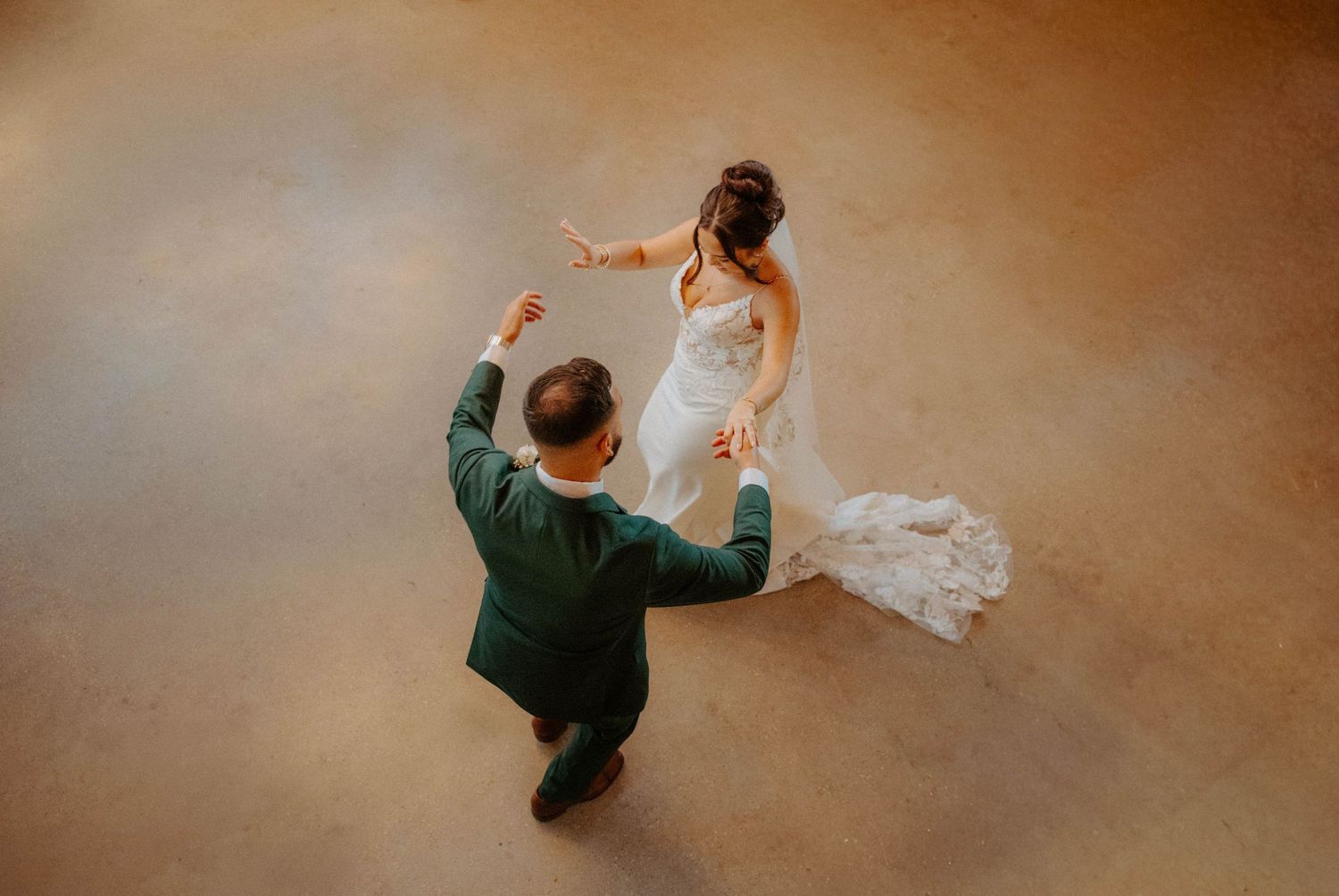 Aerial view of bride and groom sharing first dance, bride in lace gown with train.