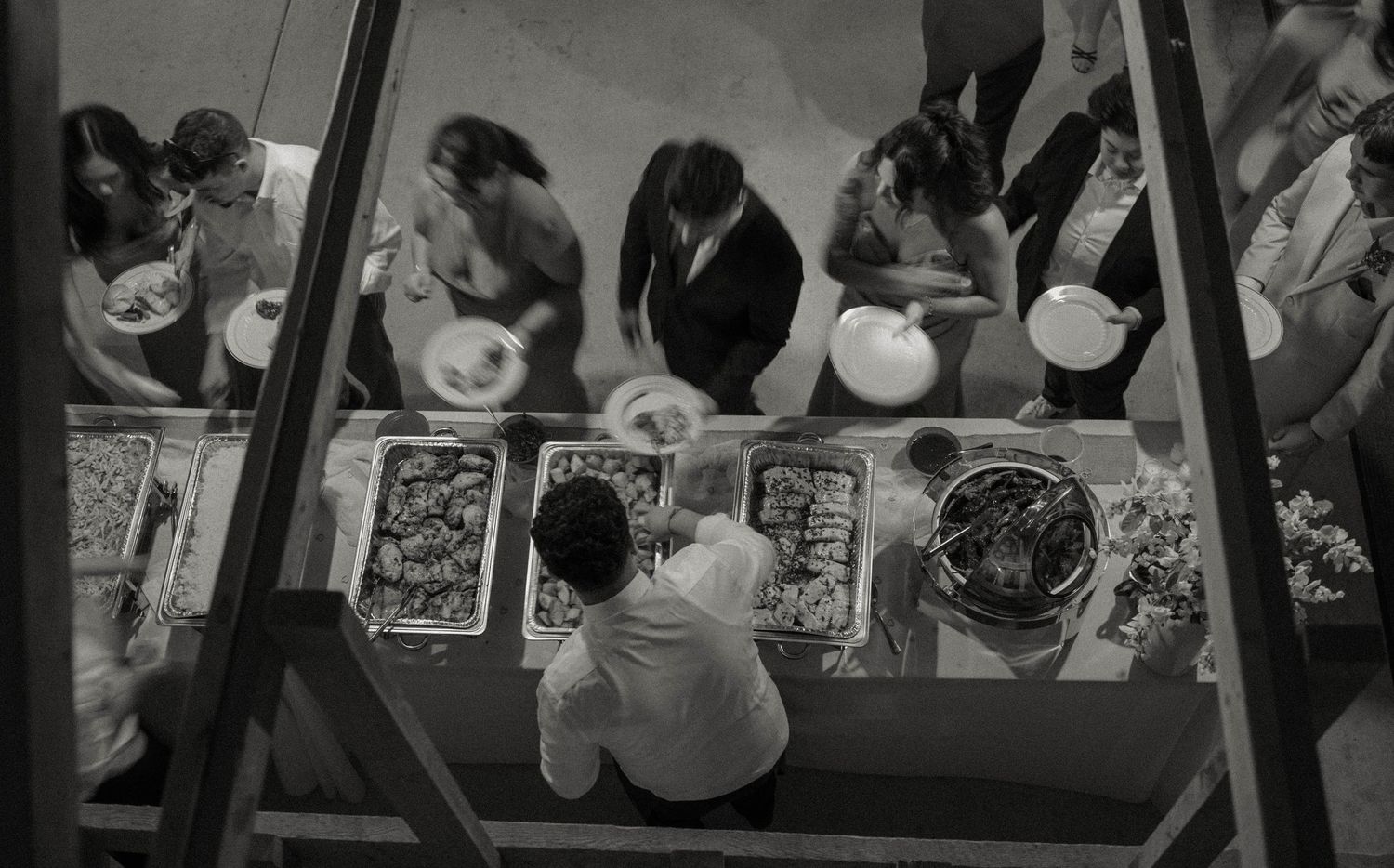 Aerial black and white view of wedding guests serving themselves at a buffet table.