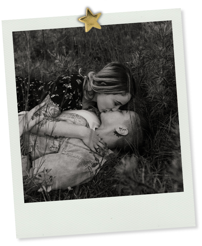 Black and white photo of a couple sharing a tender kiss while lying in a grassy field.