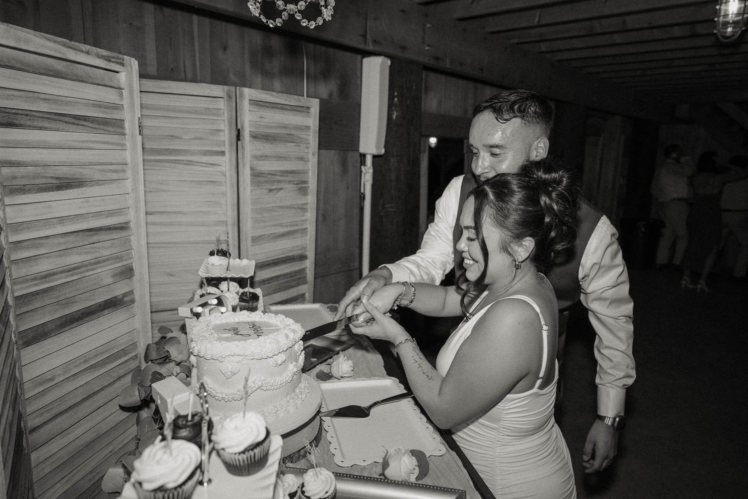 Black and white photo of bride and groom cutting wedding cake together at reception.