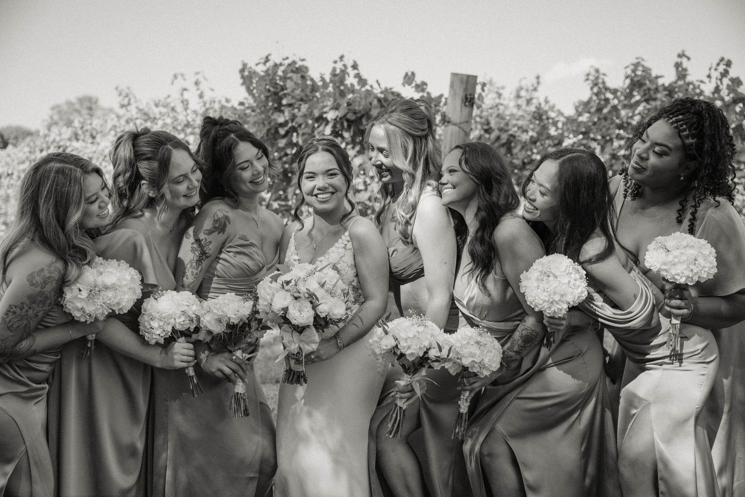 Black and white photo of bride laughing with bridesmaids holding white bouquets outdoors.