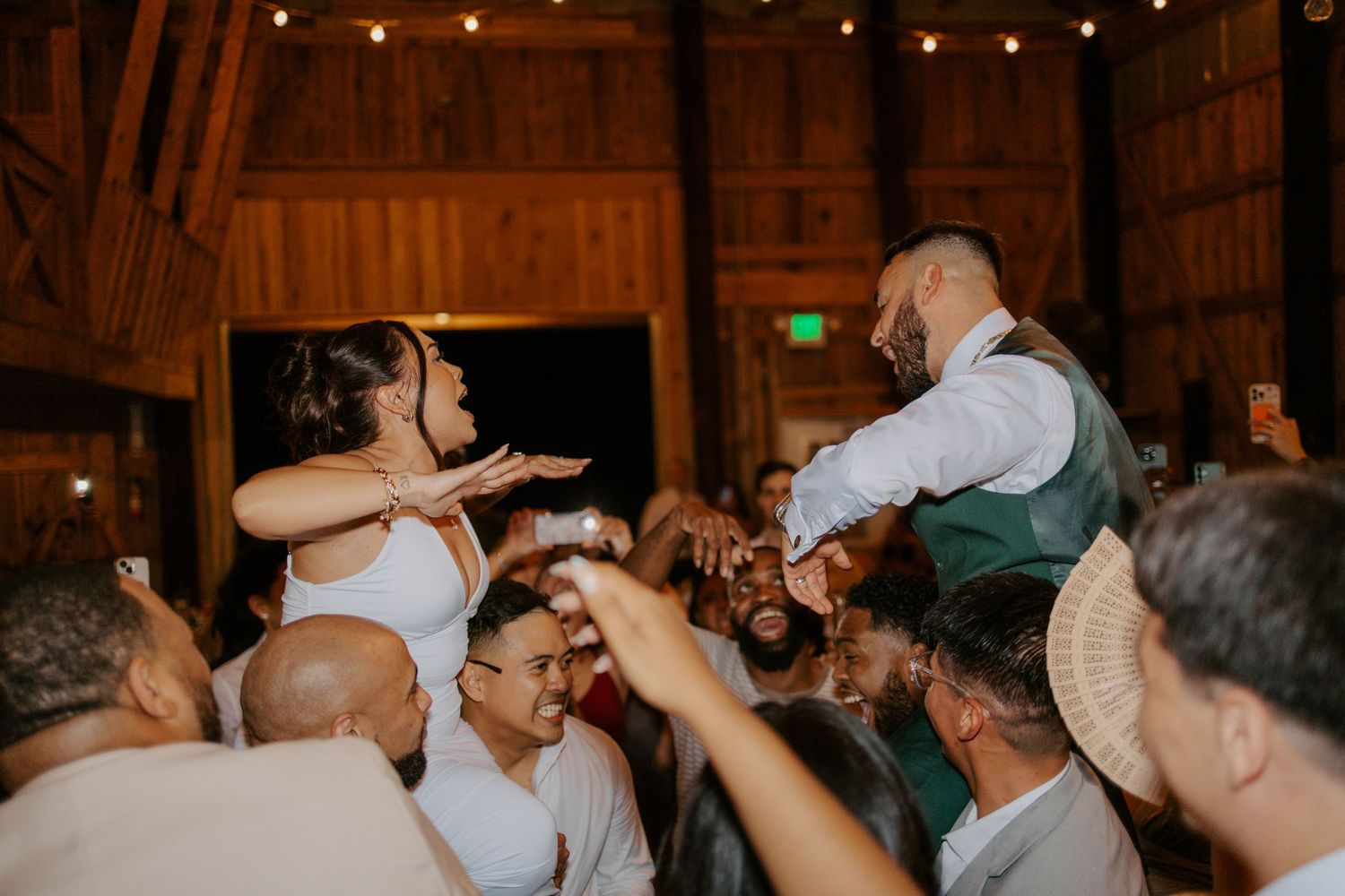 Bride and groom lifted by guests during energetic barn wedding reception dance.