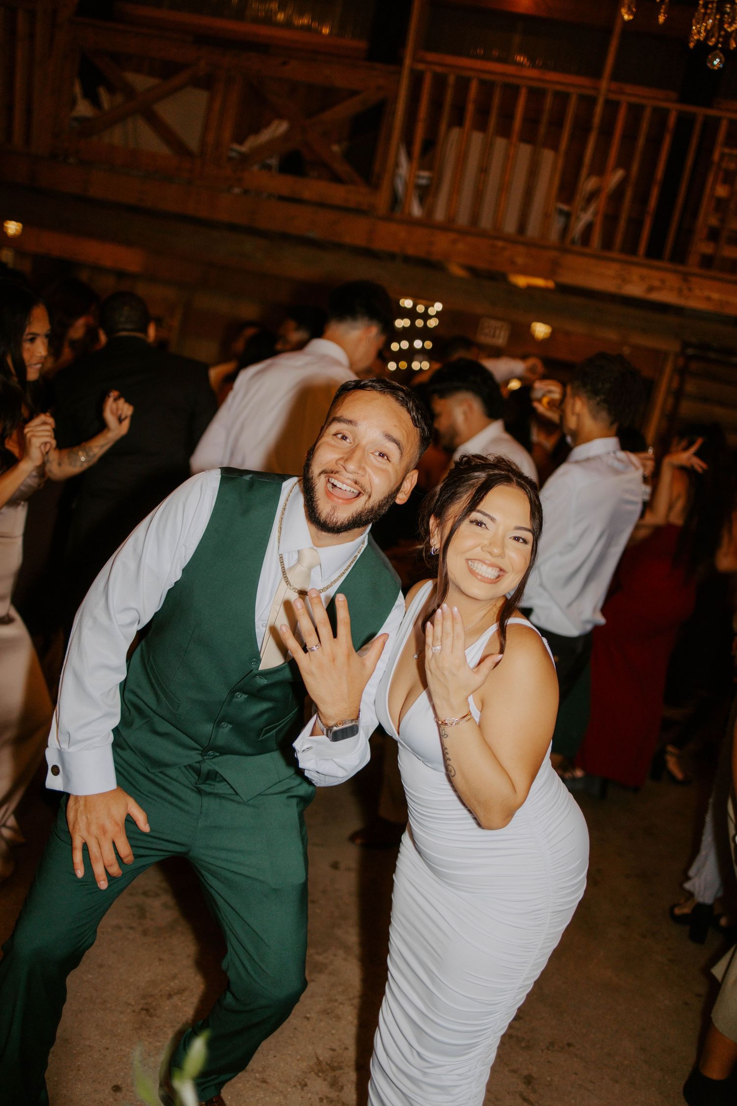 Bride and groom showing wedding rings while dancing at lively barn reception.