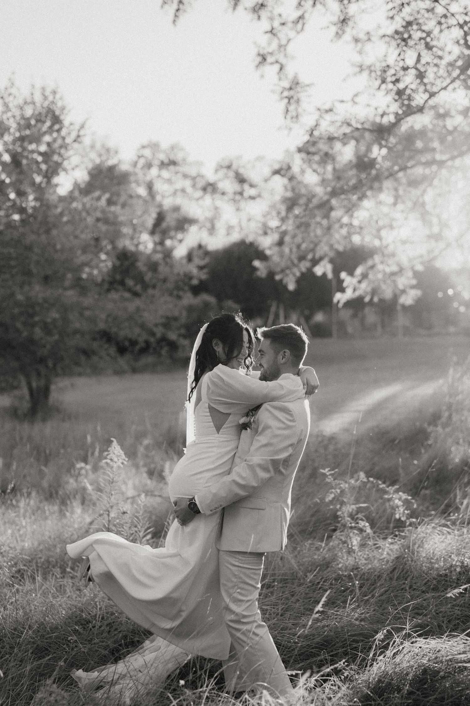 Groom lifting bride in wedding attire during golden hour outdoor portrait.