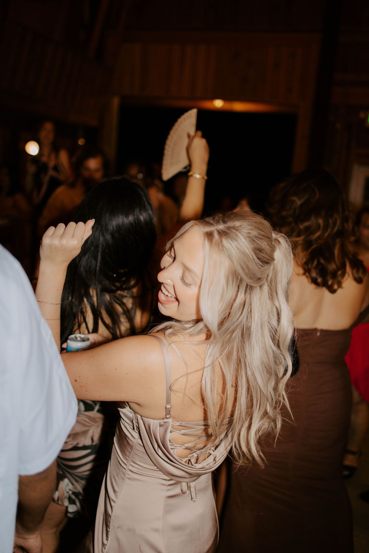 Two women in satin dresses dancing and embracing on a crowded wedding reception dance floor.