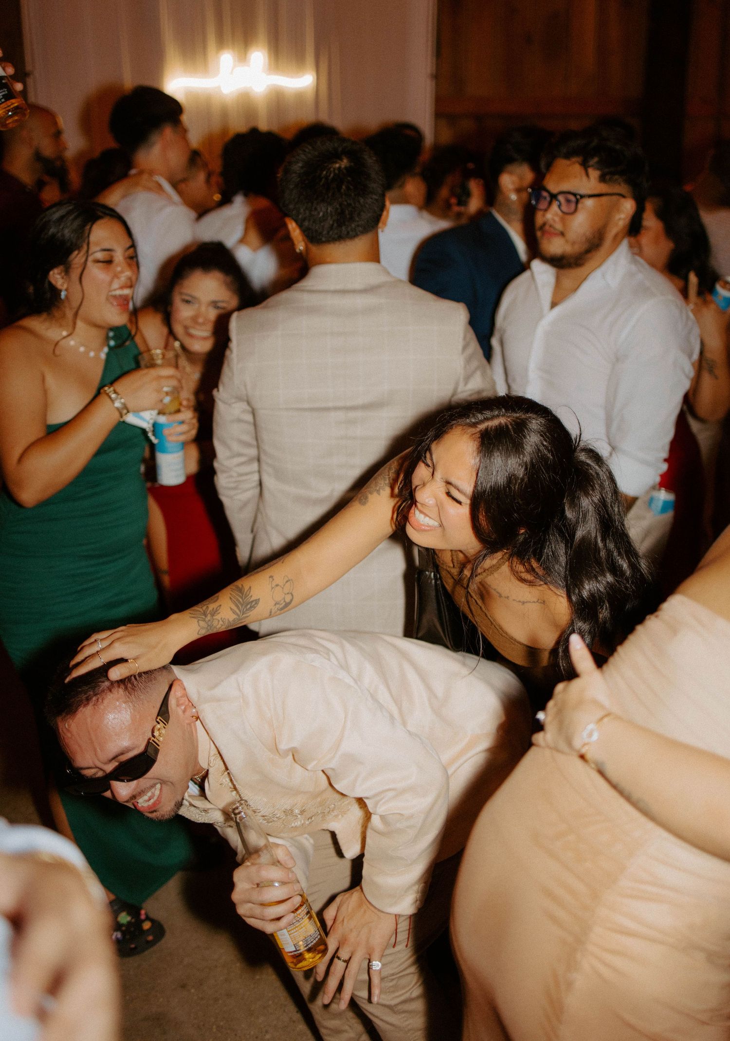 Wedding guests dancing and celebrating joyfully at a lively indoor reception party.