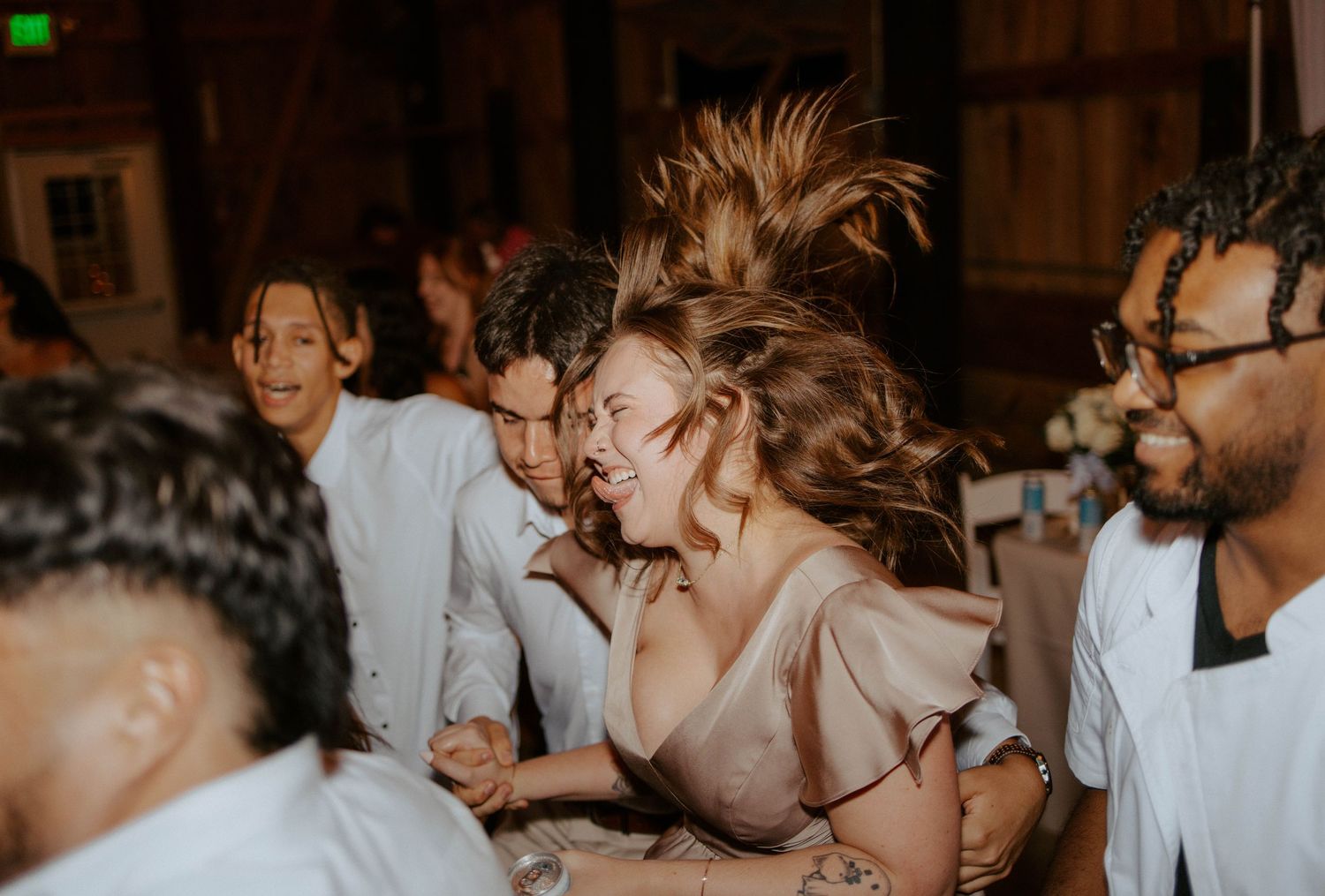 Wedding guest with hair flying while dancing energetically at a dimly lit reception.
