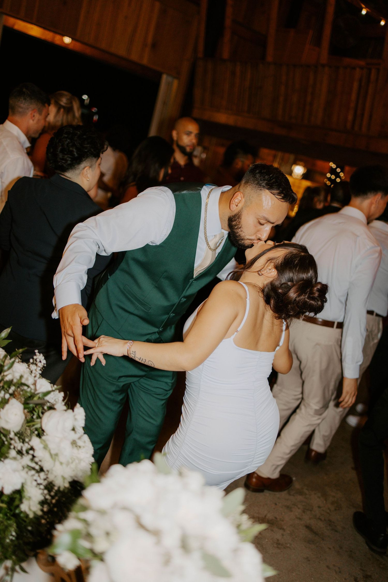 Couple sharing a romantic kiss on the wedding reception dance floor, groom in green vest.