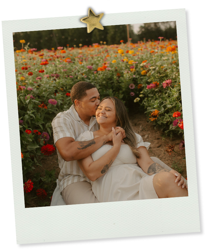 Couple sharing a sweet embrace while sitting in a vibrant colorful flower field during golden hour.