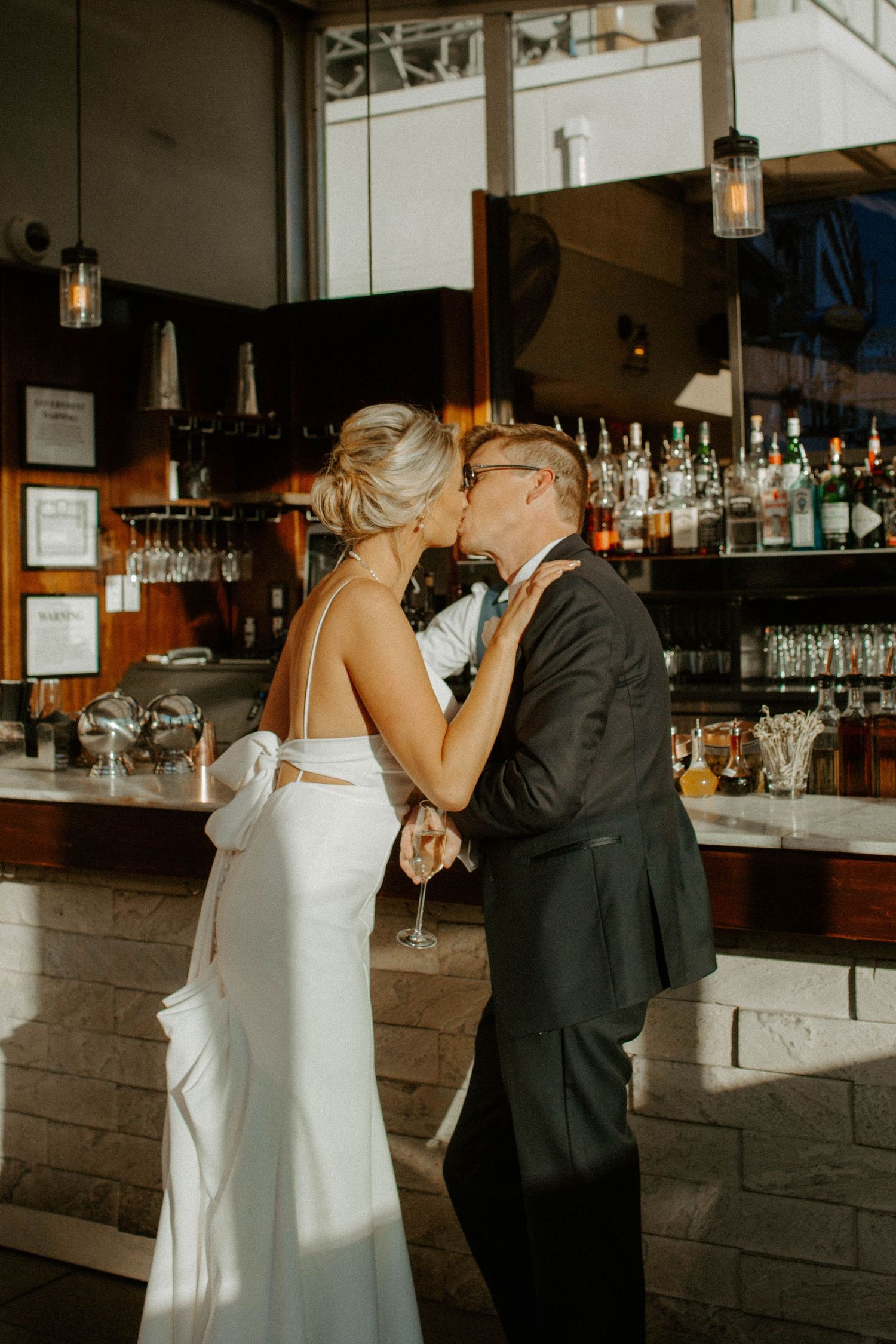 Bride and groom share a romantic kiss at a bar during their wedding reception.