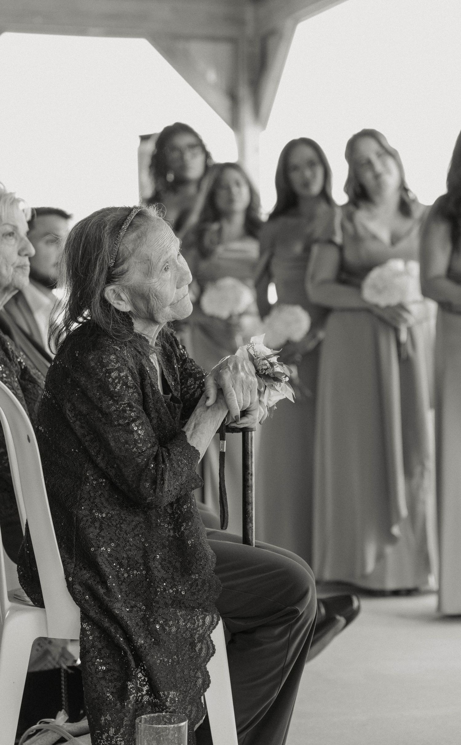 Emotional elderly woman clasping hands watching wedding ceremony in black and white photo.