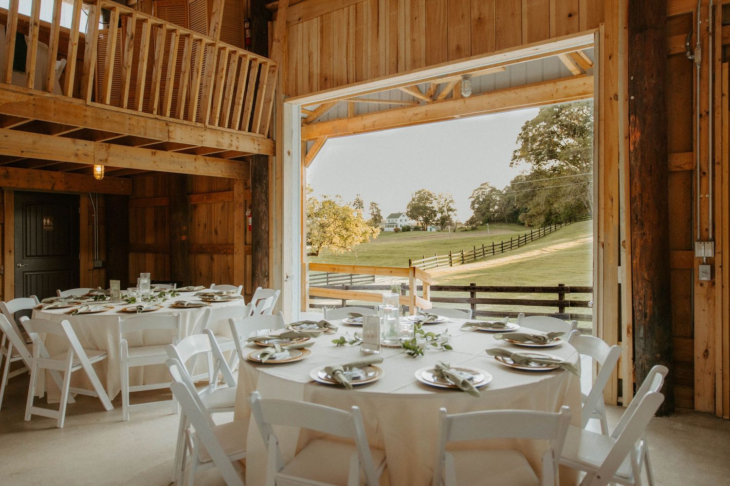 Elegant barn wedding reception with white round tables, folding chairs, and scenic countryside views.