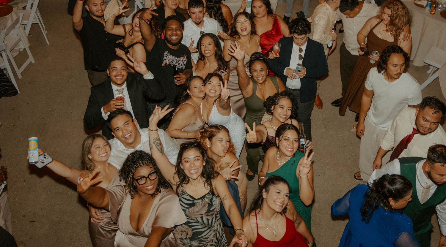 Large group of smiling wedding guests posing together on the dance floor at reception.