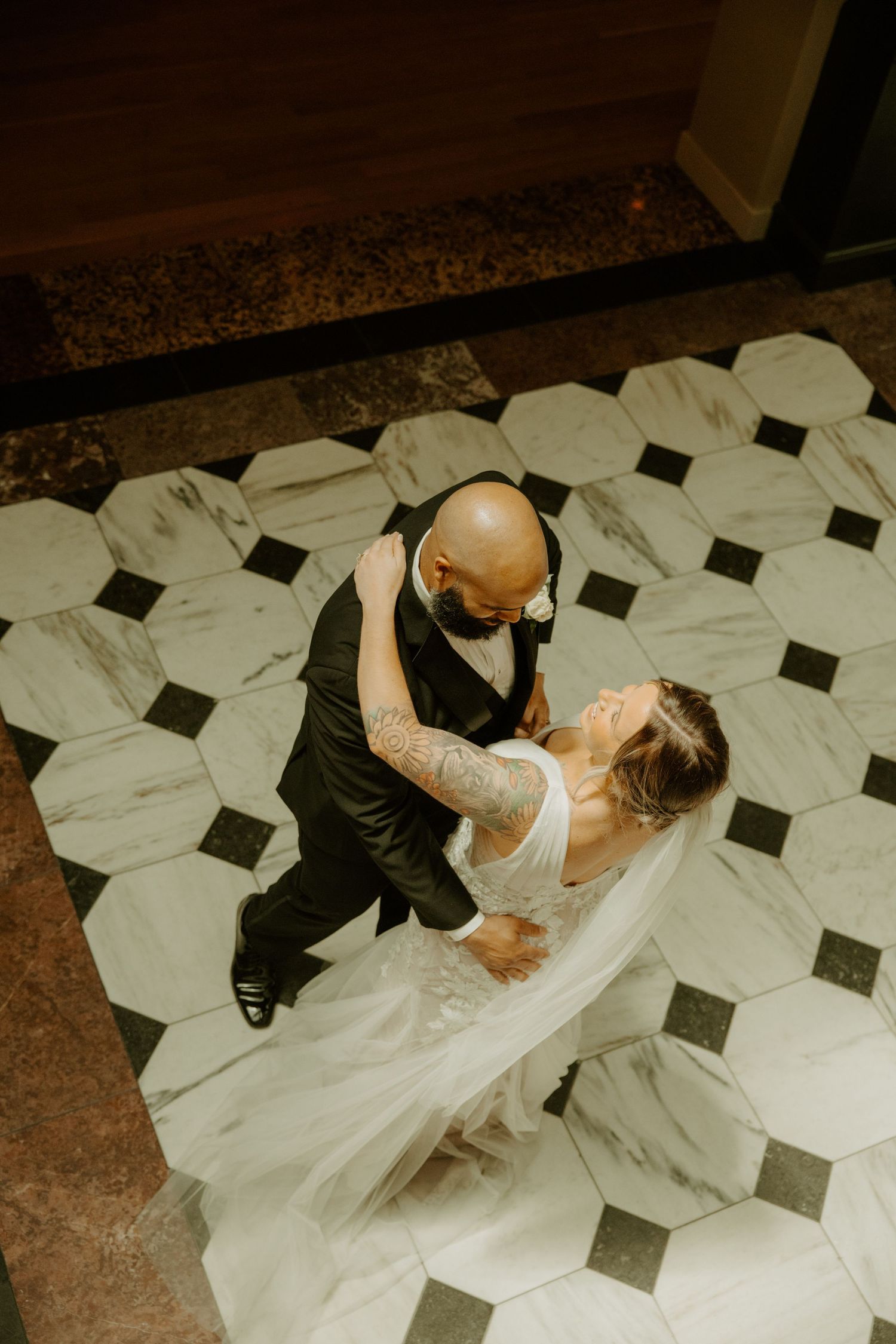 Bride and groom share first dance on marble hexagon tile floor, aerial view of wedding couple embracing.