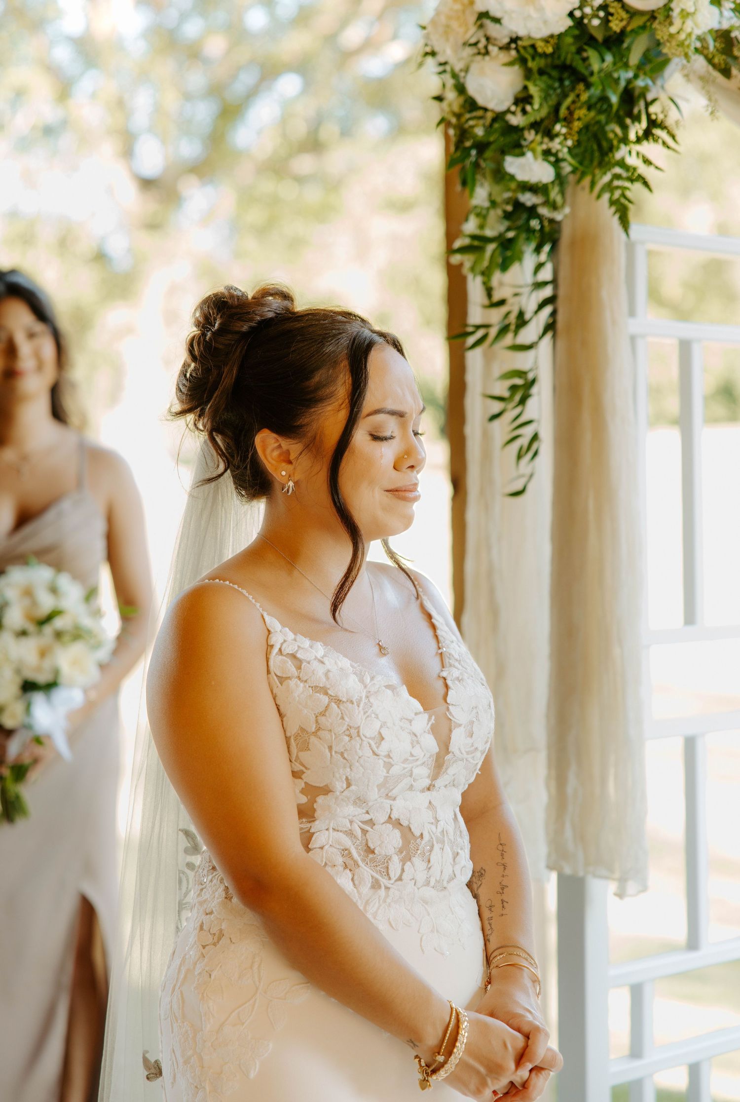 Beautiful bride in lace gown with eyes closed peacefully at outdoor wedding ceremony altar.