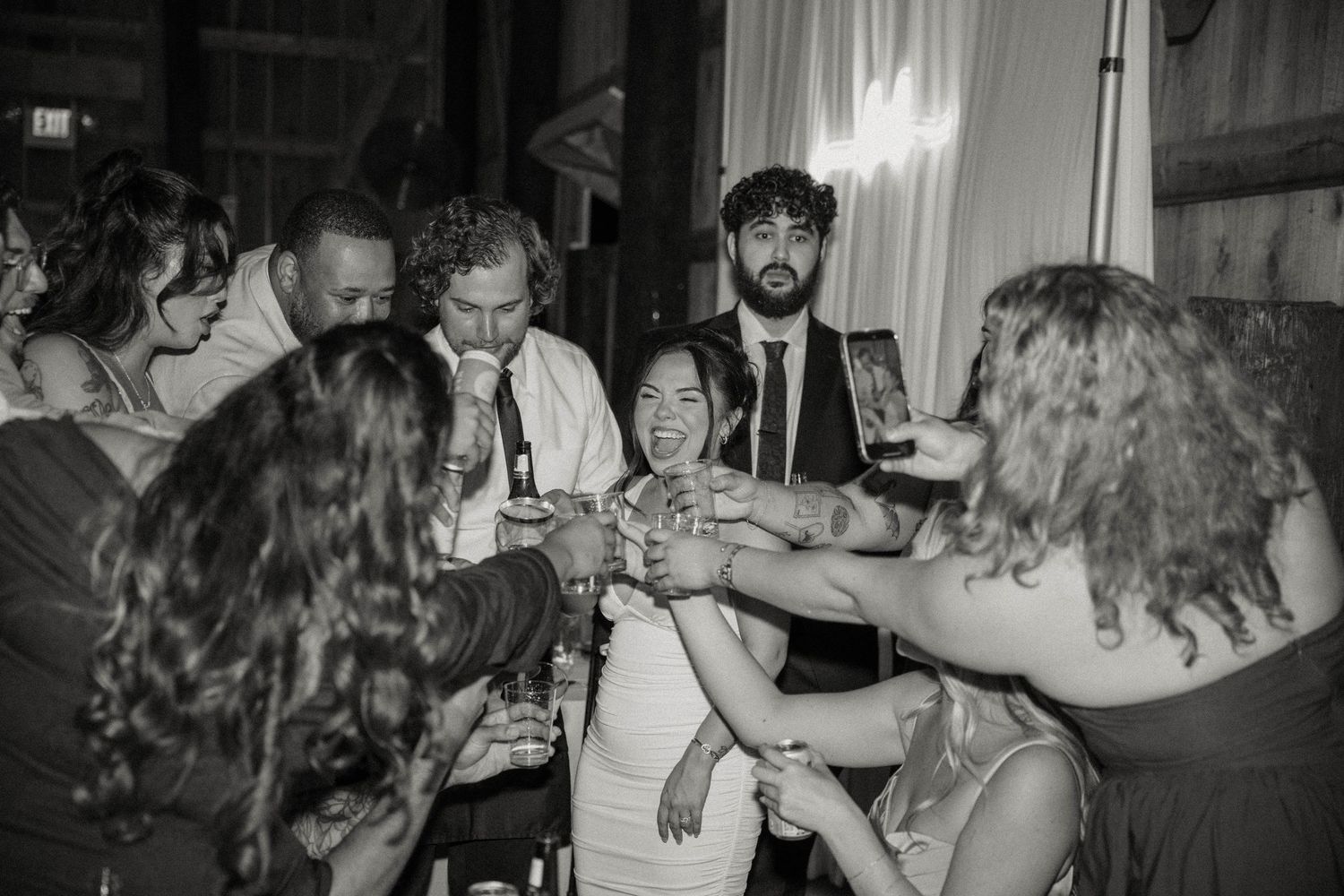 Black and white photo of wedding guests toasting drinks together on the dance floor.