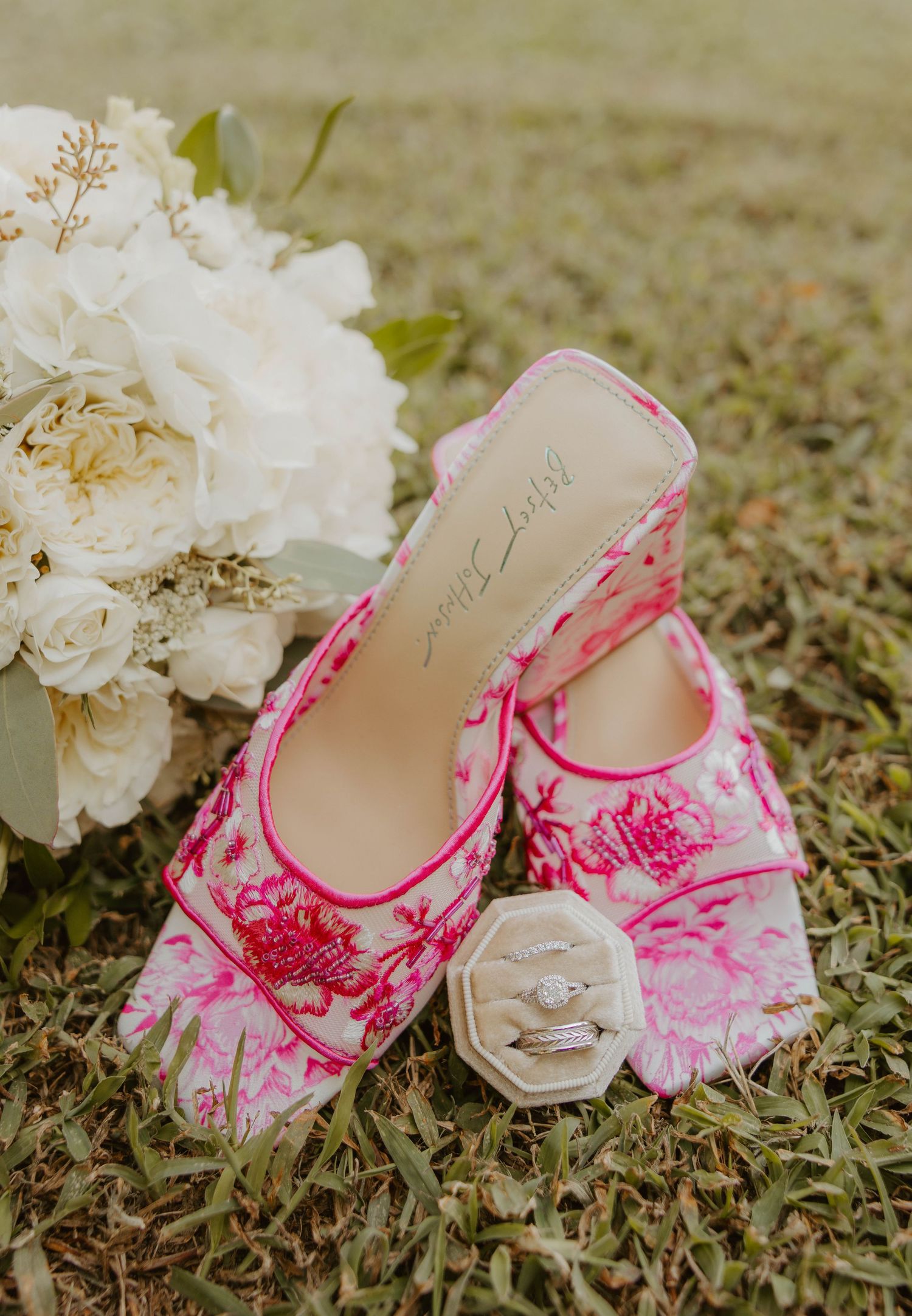 Pink floral embroidered bridal heels with diamond ring box beside white peony wedding bouquet.