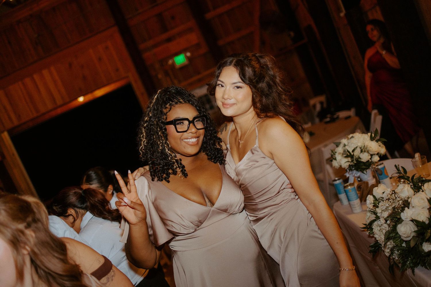 Two bridesmaids in mauve satin dresses posing together at a wedding reception venue.
